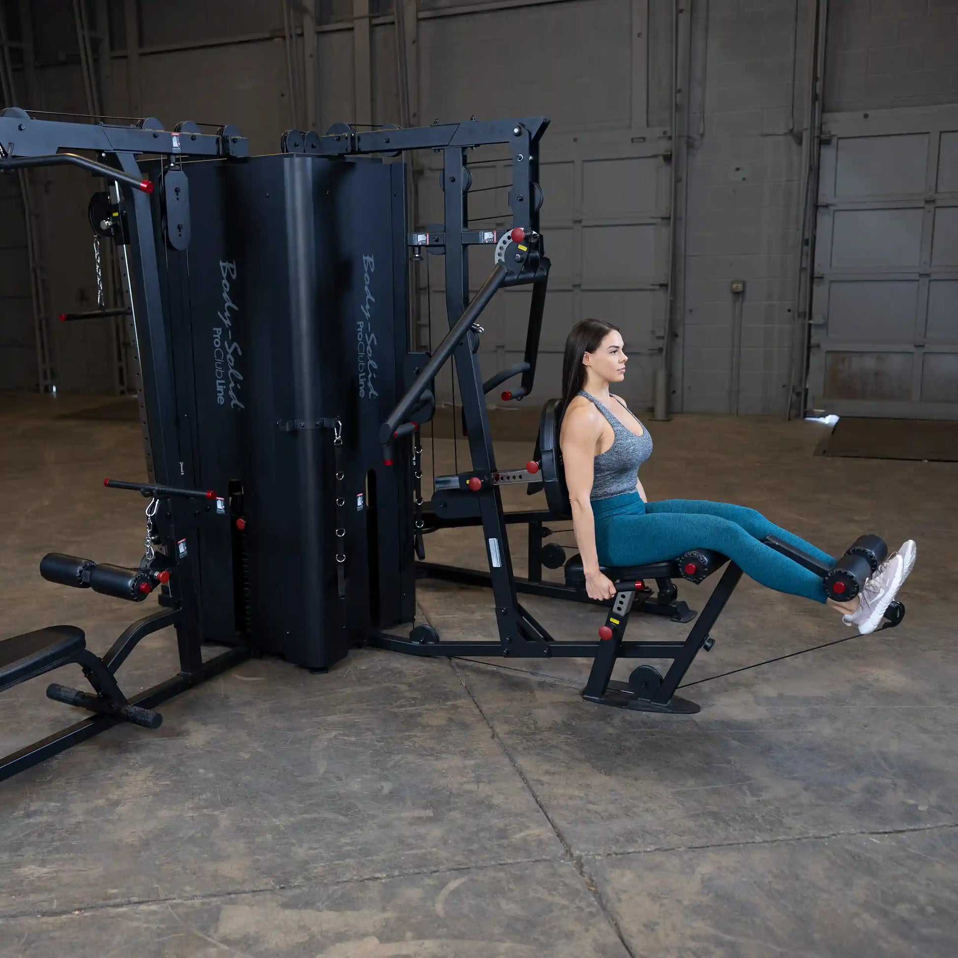 A woman using the Body-Solid Pro ClubLine Four-Stack Gym S1000, performing a seated exercise in a spacious gym environment.
