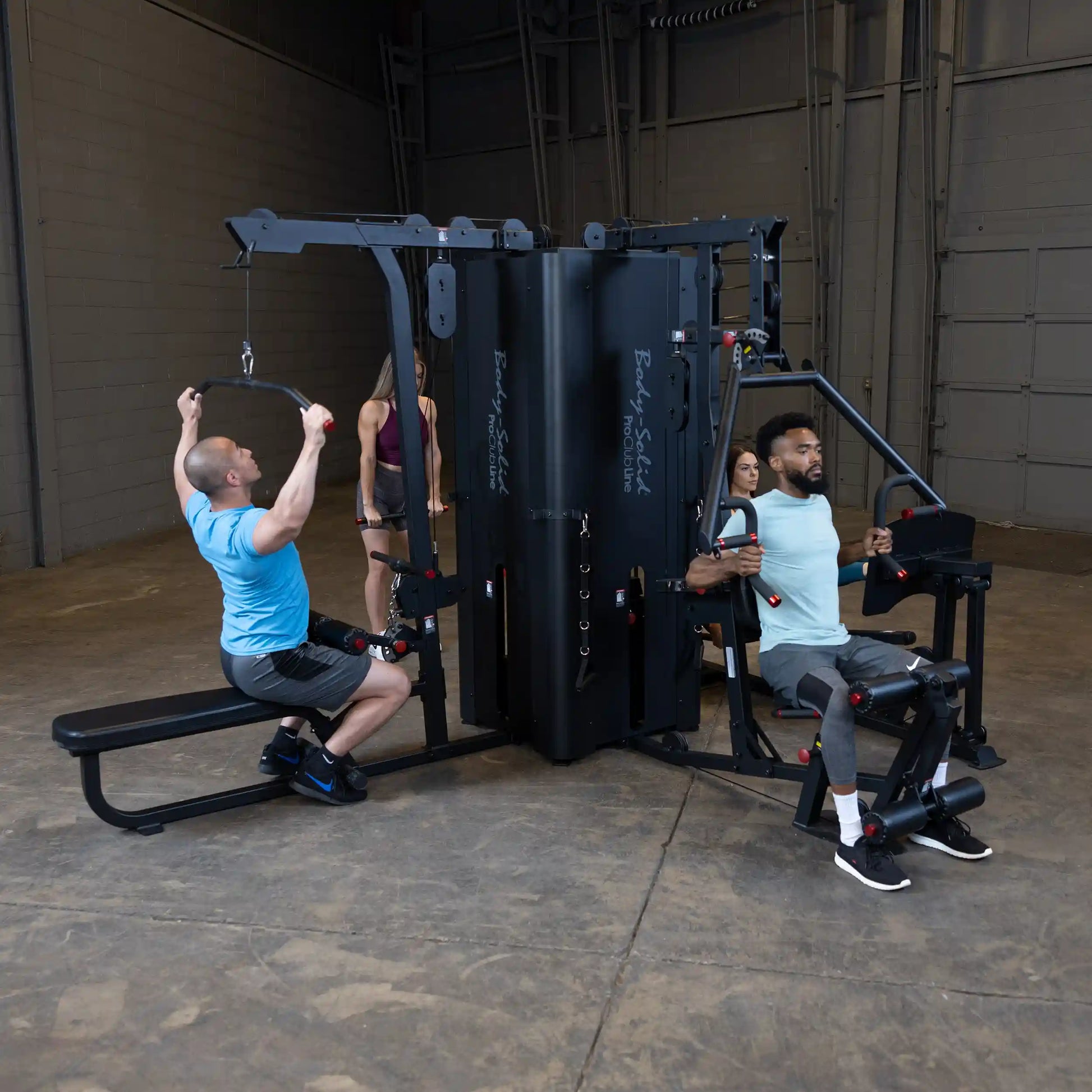 Two individuals using the Body-Solid Pro ClubLine Four-Stack Gym S1000, one performing a lat pulldown and the other engaged in a seated row, in a spacious gym setting.