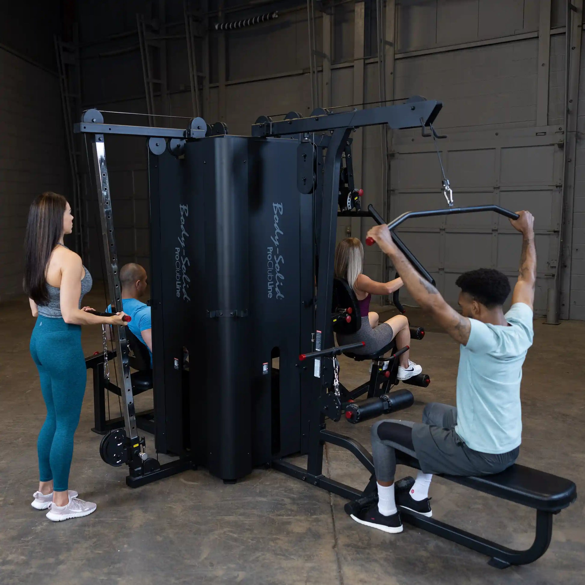 A fitness gym scene featuring the Body-Solid Pro ClubLine Four-Stack Gym S1000, with three individuals using the equipment for various exercises.
