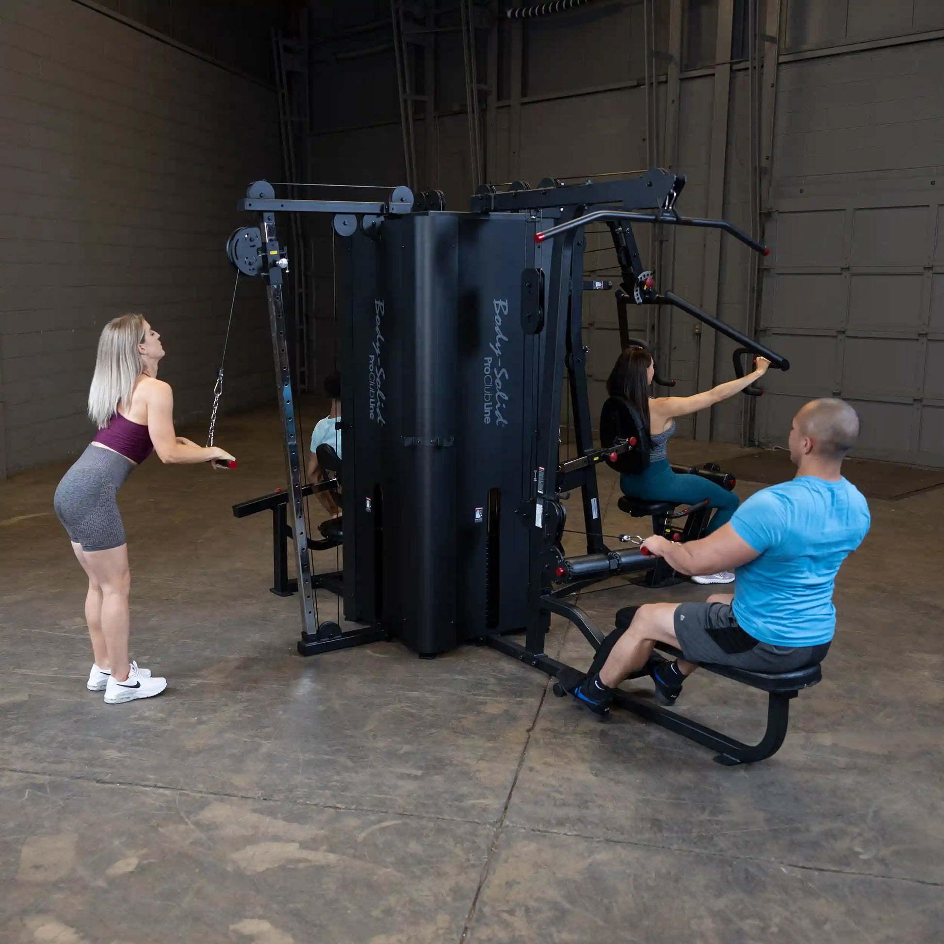 Three individuals using the Body-Solid Pro ClubLine Four-Stack Gym S1000 in a spacious gym setting, engaging in various exercises.