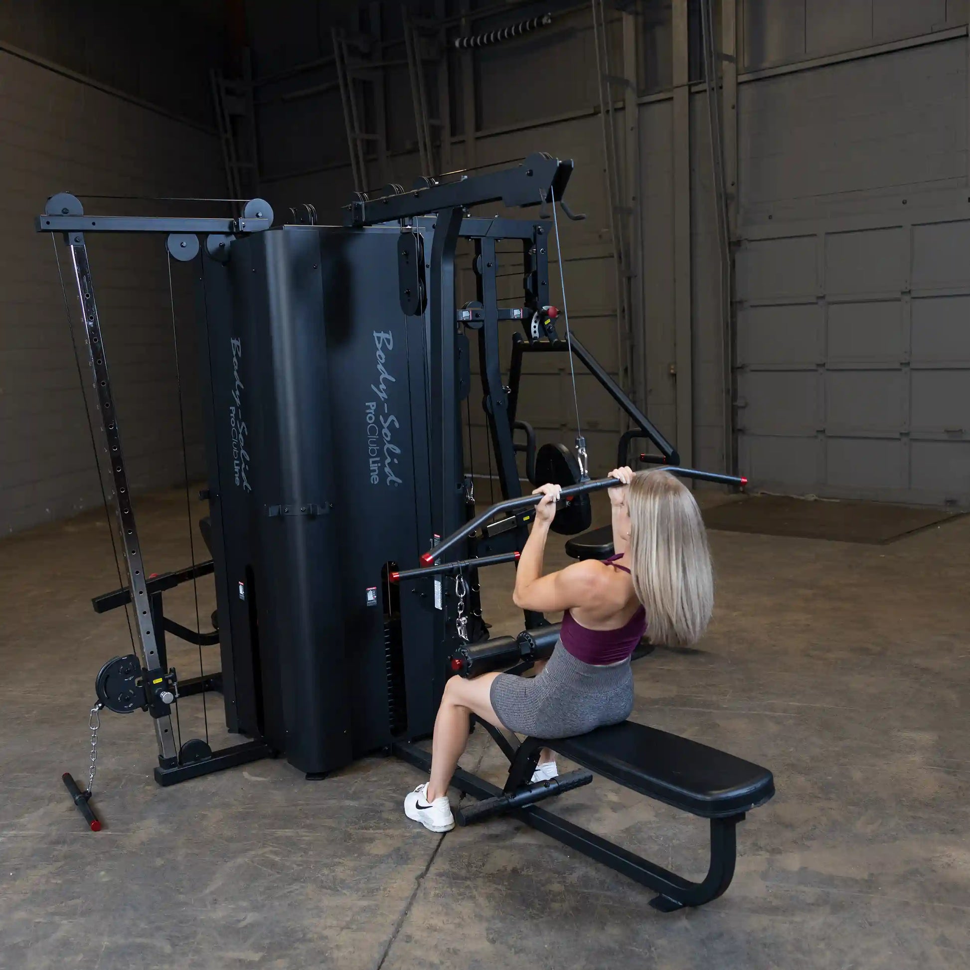 A person using the Body-Solid Pro ClubLine Four-Stack Gym S1000, performing a seated exercise with a bar attachment in a spacious gym environment.