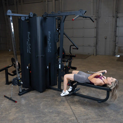 A person using the Body-Solid Pro ClubLine Four-Stack Gym S1000, performing an exercise while lying on a bench, in a spacious gym setting.