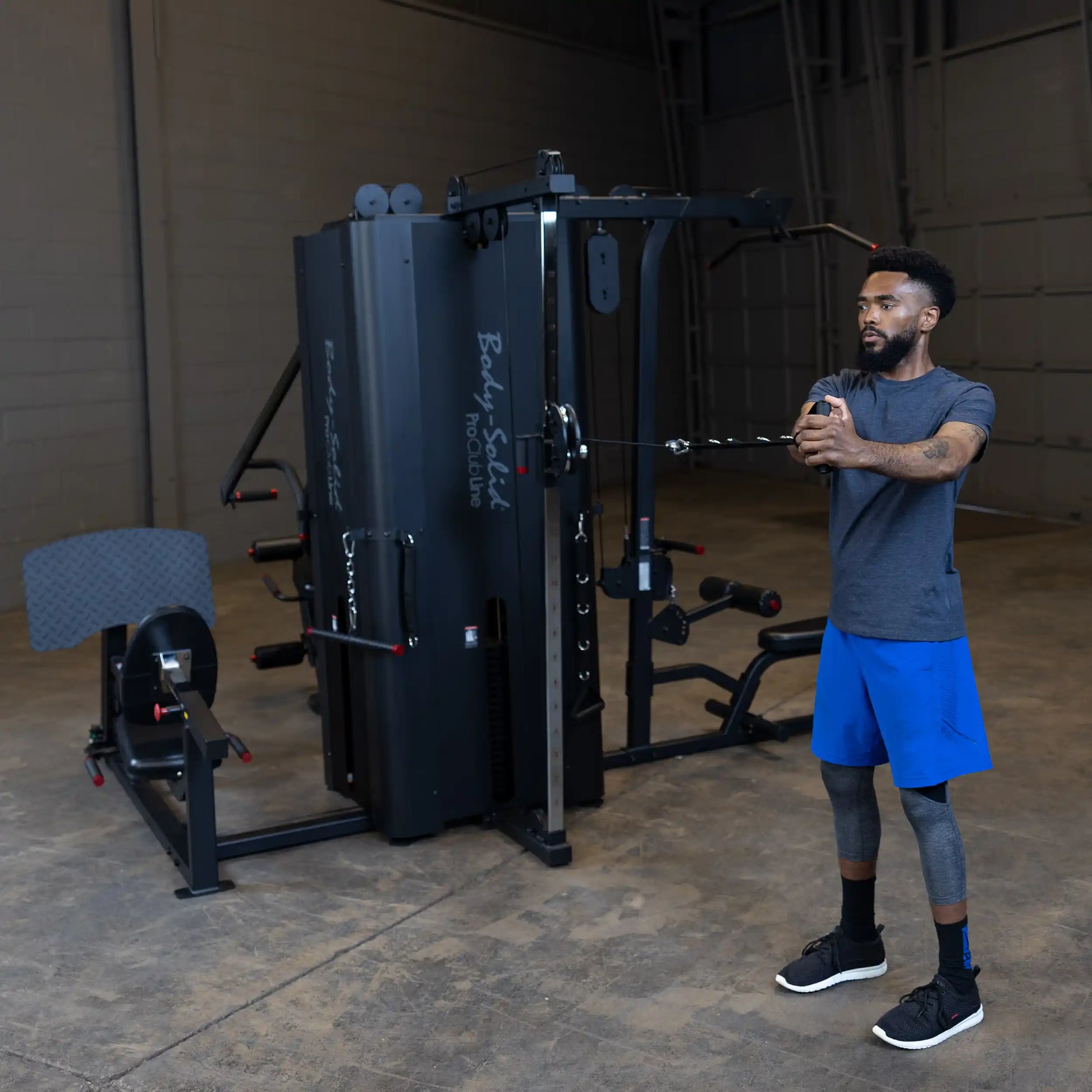A person using the Body-Solid Pro ClubLine Four-Stack Gym S1000, performing an exercise with a cable attachment in a spacious gym setting.