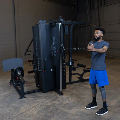 A person using the Body-Solid Pro ClubLine Four-Stack Gym S1000, performing an exercise with a cable attachment in a spacious gym setting.