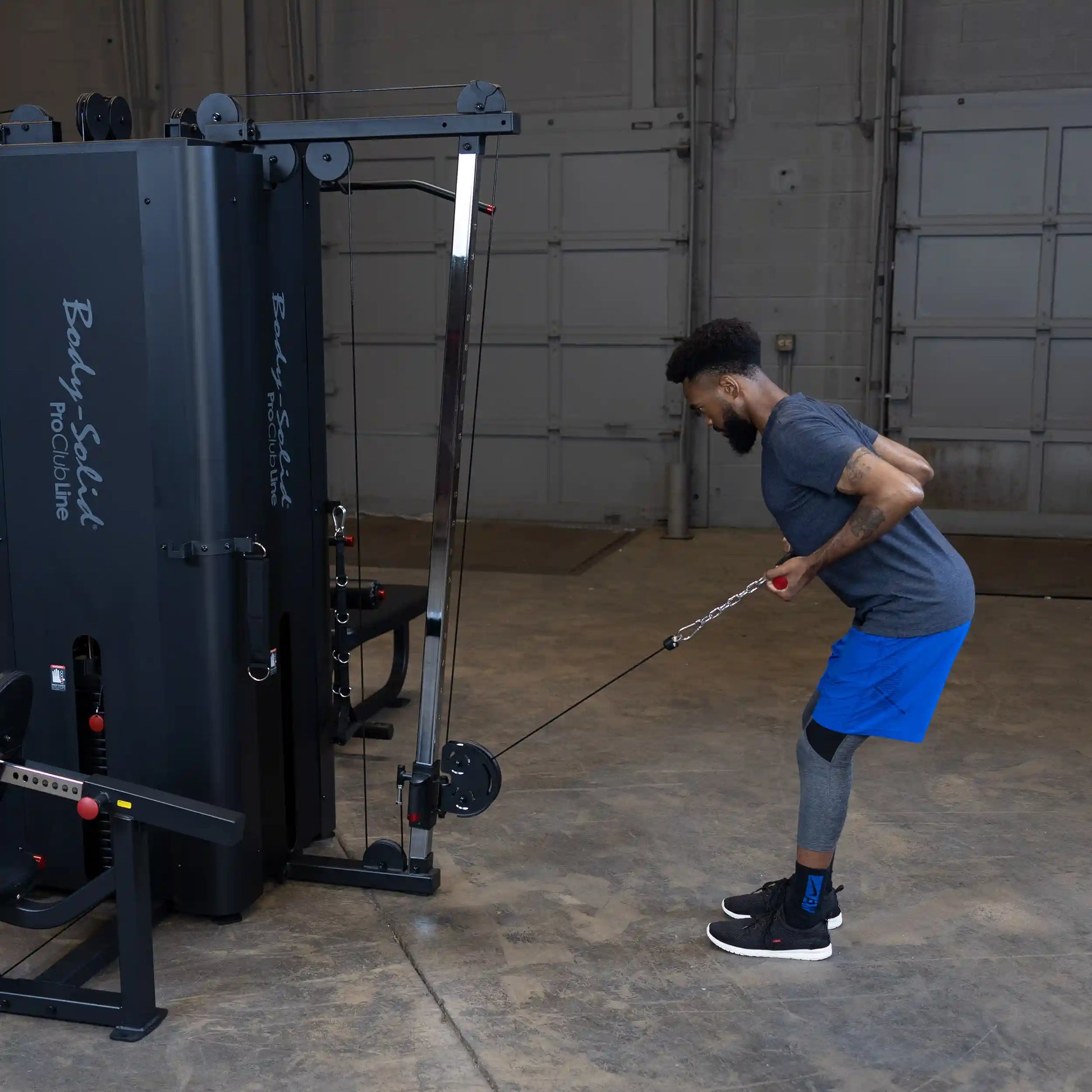 A person using the Body-Solid Pro ClubLine Four-Stack Gym S1000, performing a cable exercise with a resistance band in a gym setting.