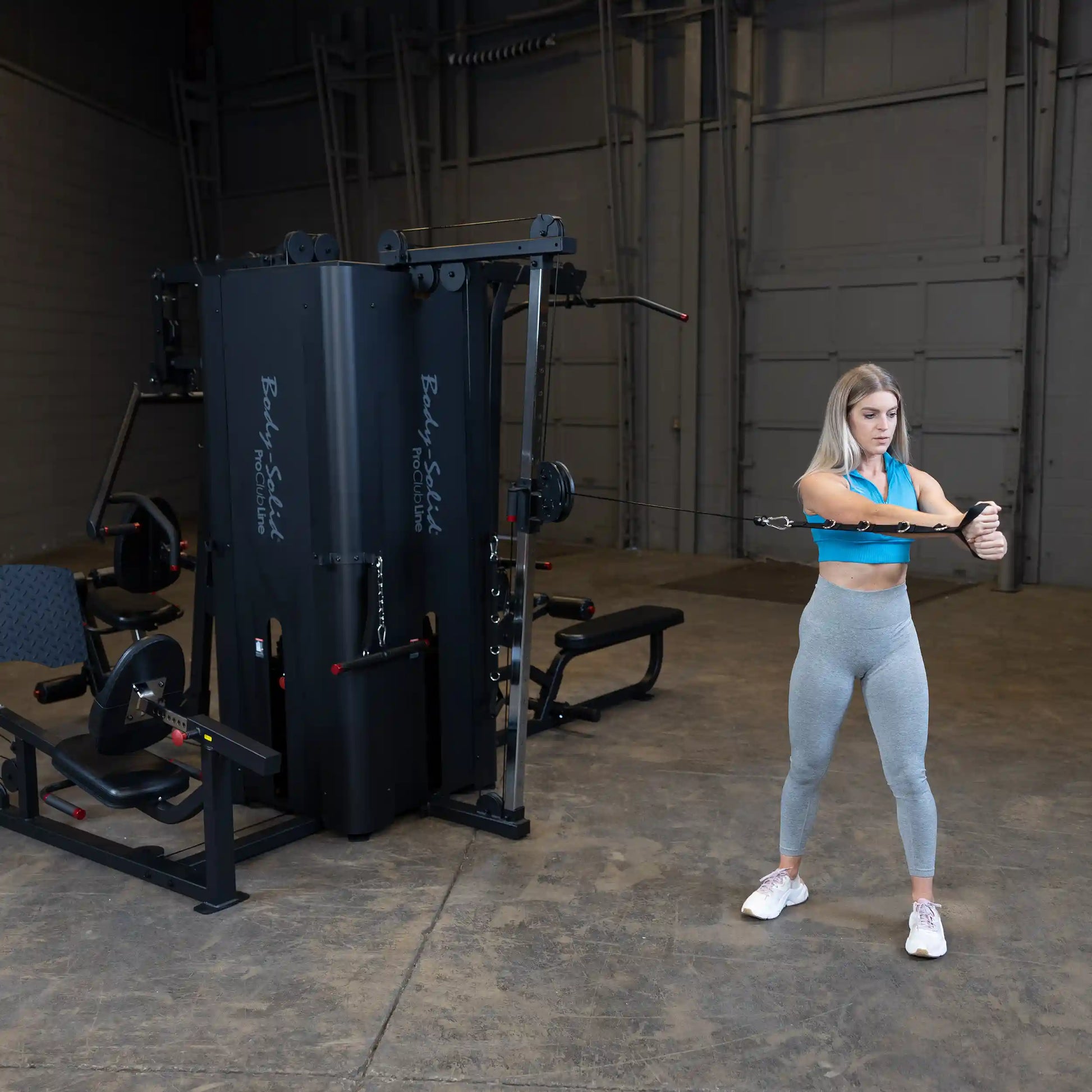 A woman in athletic wear using the Body-Solid Pro ClubLine Four-Stack Gym S1000 for strength training in a spacious gym setting.
