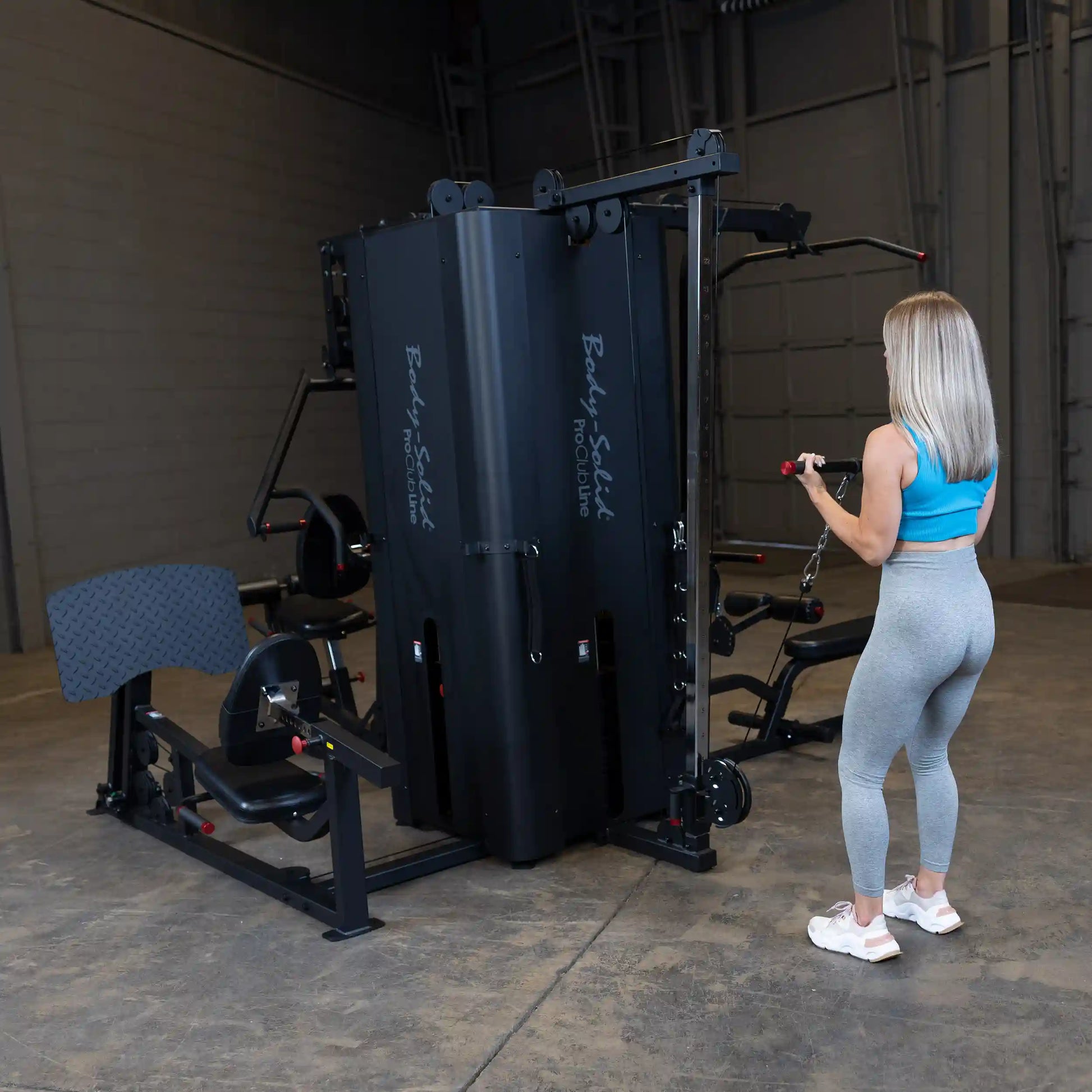 A woman using the Body-Solid Pro ClubLine Four-Stack Gym S1000, performing an exercise in a spacious gym environment.
