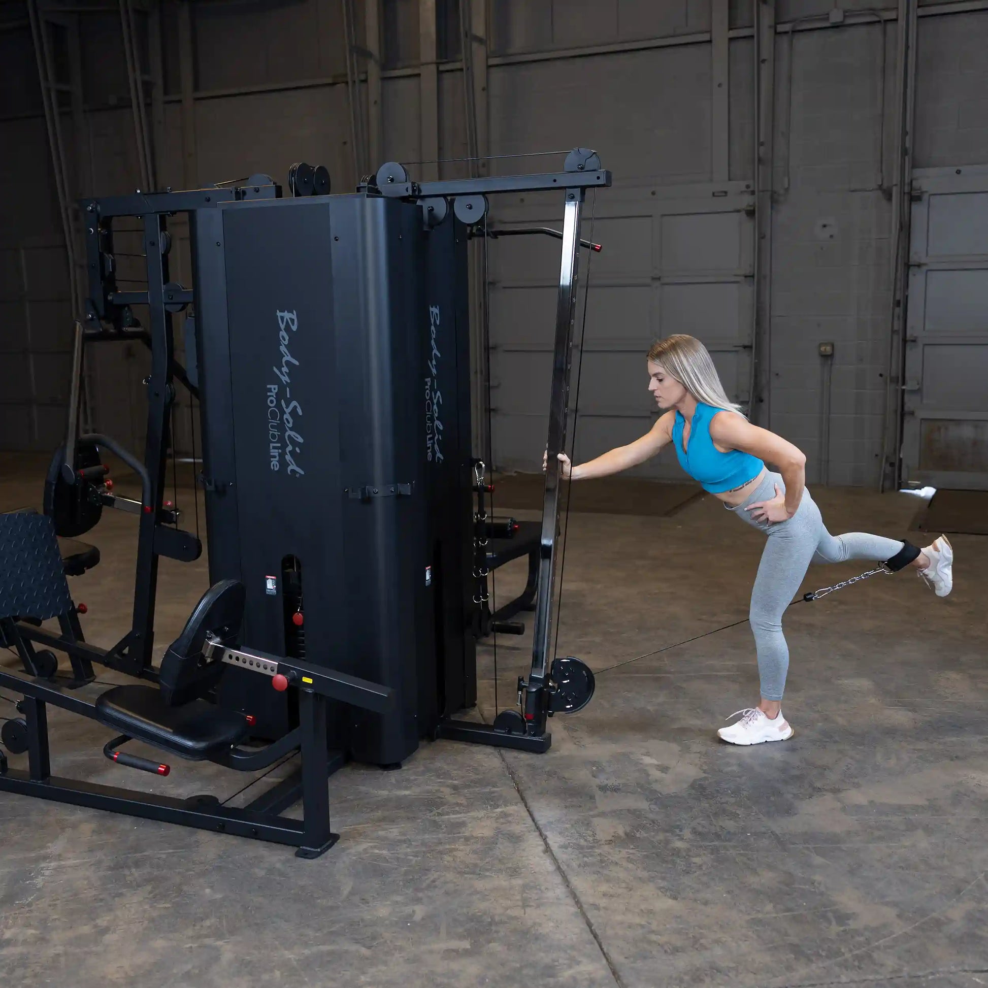 A woman performs an exercise using the Body-Solid Pro ClubLine Four-Stack Gym S1000 in a spacious gym setting.