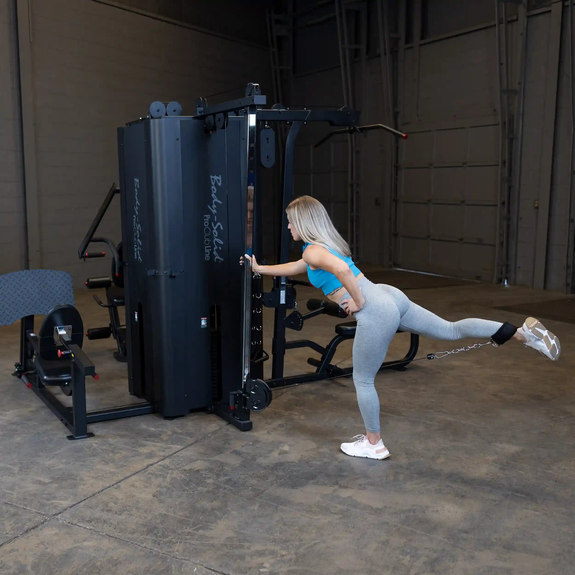 A person using the Body-Solid Pro ClubLine Four-Stack Gym S1000 for a leg exercise, demonstrating proper form in a gym setting.