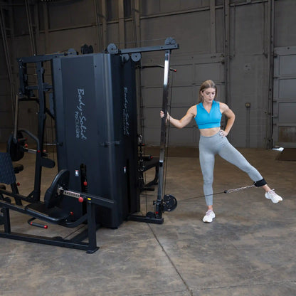 Woman exercising with the Body-Solid Pro ClubLine Four-Stack Gym S1000, performing a leg lift while using a cable attachment in a spacious gym setting.