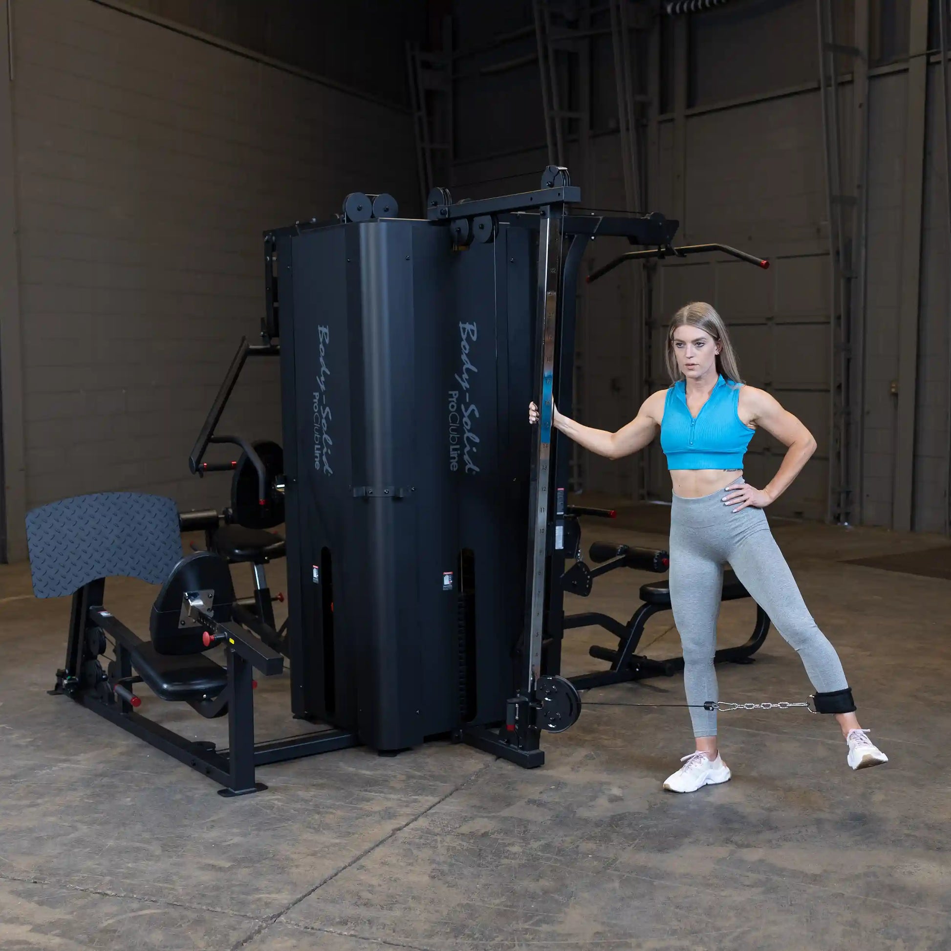 A woman demonstrating an exercise using the Body-Solid Pro ClubLine Four-Stack Gym S1000 in a spacious gym setting.