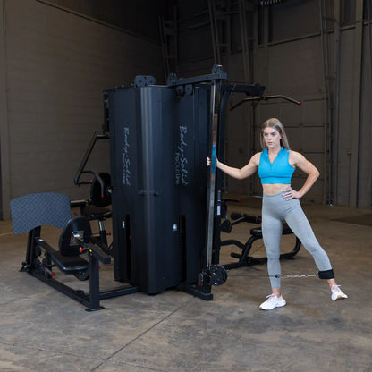 A woman demonstrating an exercise using the Body-Solid Pro ClubLine Four-Stack Gym S1000 in a spacious gym setting.