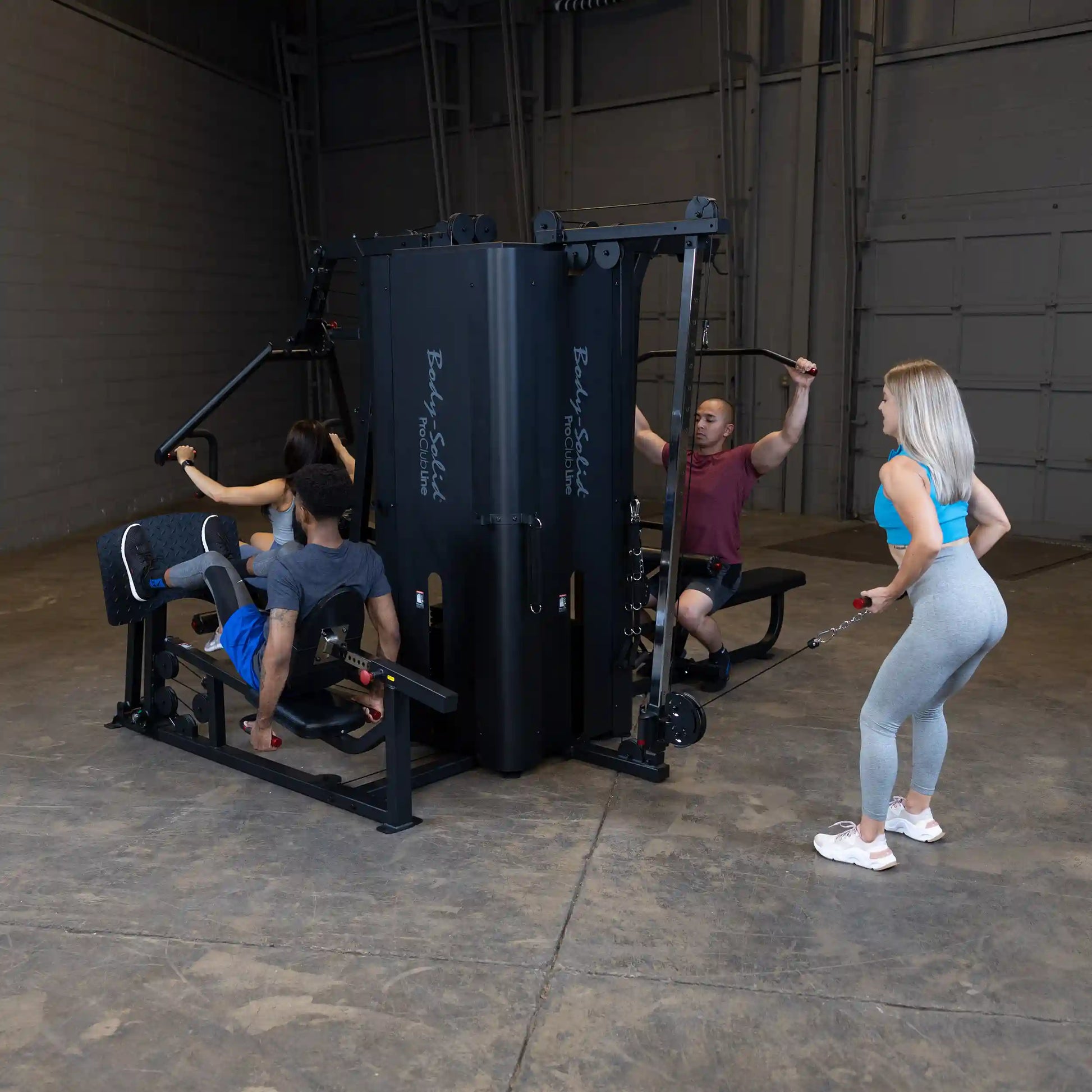 Three individuals using the Body-Solid Pro ClubLine Four-Stack Gym S1000 in a spacious gym setting, engaged in various exercises.