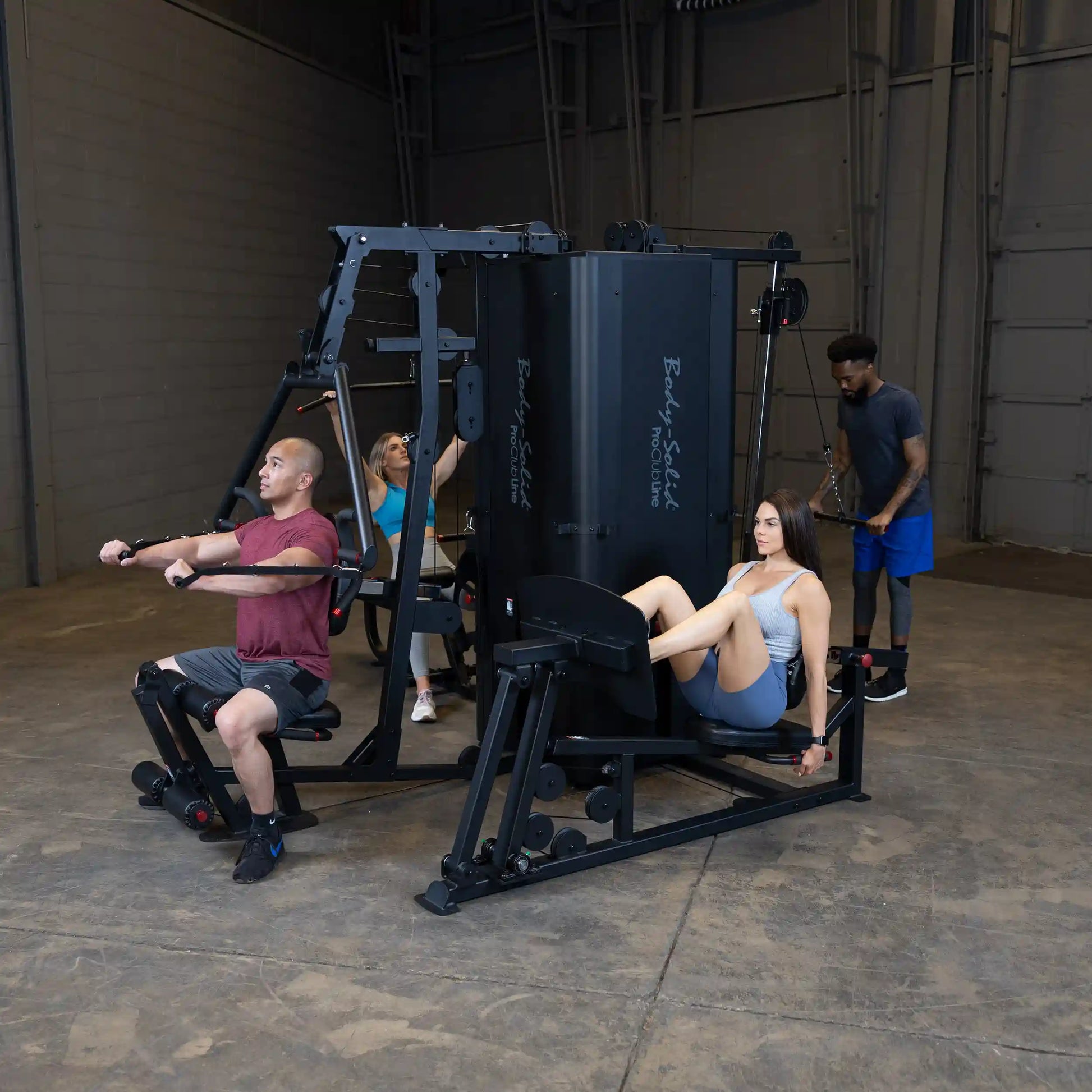 Group of individuals exercising on the Body-Solid Pro ClubLine Four-Stack Gym S1000, featuring a man performing a rowing motion, a woman using a leg press, and two others engaged in different workouts in a gym setting.