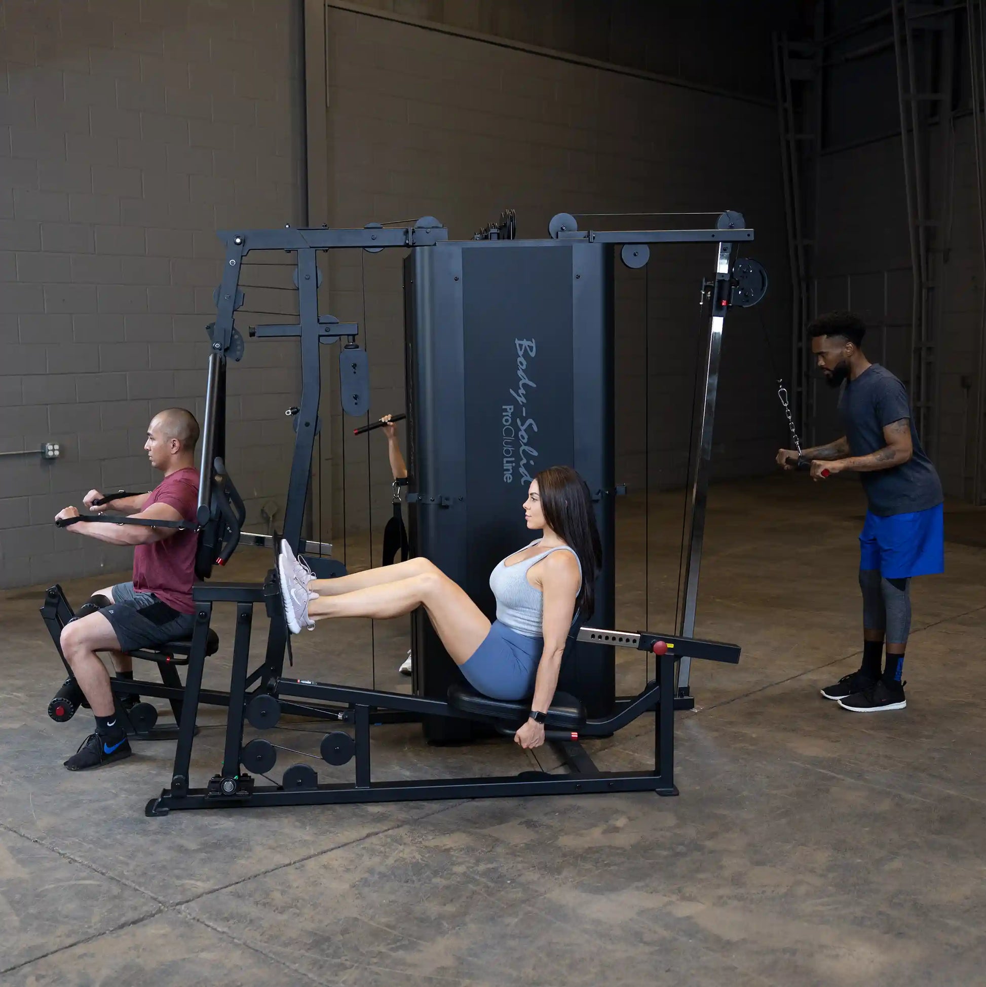 Three individuals exercising using the Body-Solid Pro ClubLine Four-Stack Gym S1000 in a spacious gym setting.
