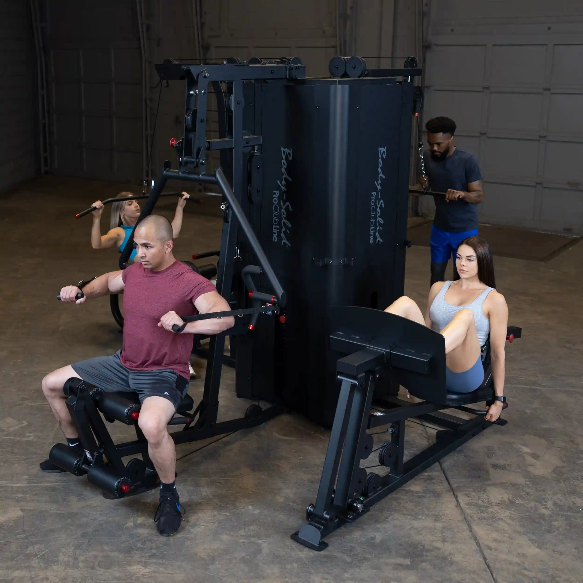 Individuals using the Body-Solid Pro ClubLine Four-Stack Gym S1000, featuring a man performing a seated row, a woman on a leg press, and another person using a pull-down machine in a gym setting.