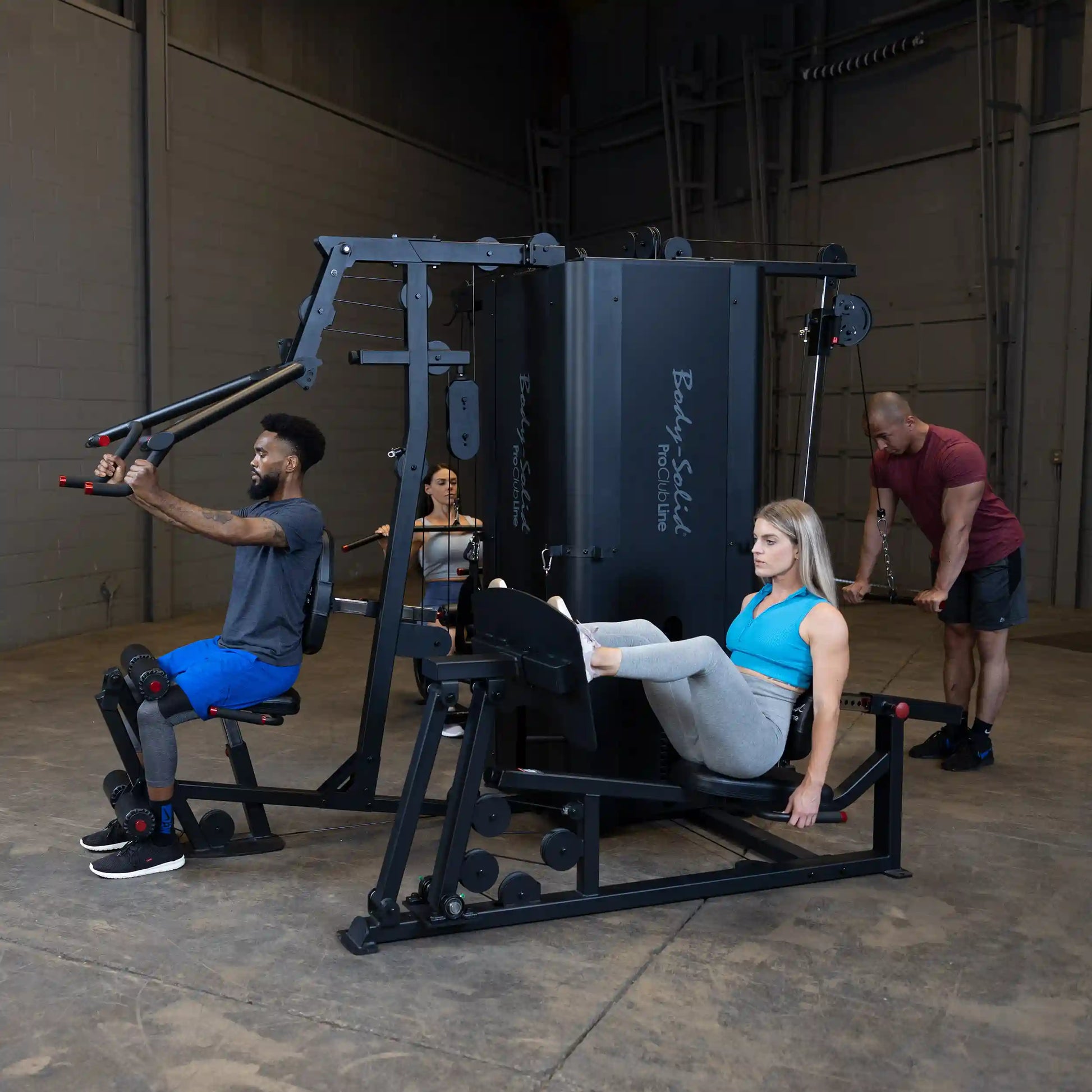 Individuals using the Body-Solid Pro ClubLine Four-Stack Gym S1000, featuring a man performing a seated row, a woman doing leg press, and another person working out in the background.