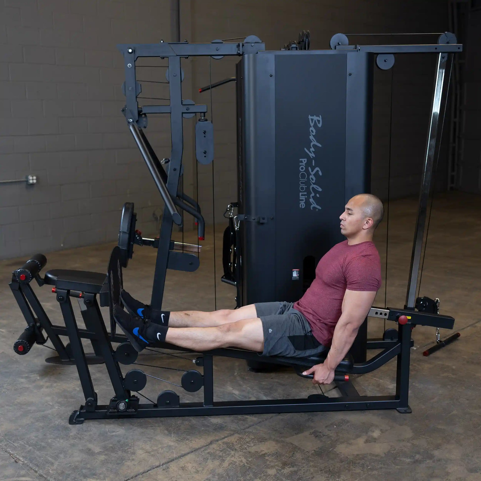 A man performing leg exercises on the Body-Solid Pro ClubLine Four-Stack Gym S1000, showcasing its various attachments and equipment in a gym setting.
