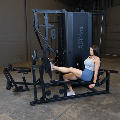 A woman exercises on the Body-Solid Pro ClubLine Four-Stack Gym S1000, using the leg extension attachment in a gym setting.