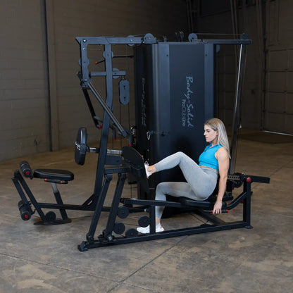 A person using the Body-Solid Pro ClubLine Four-Stack Gym S1000, engaging in a leg exercise while seated on the machine in a spacious gym setting.