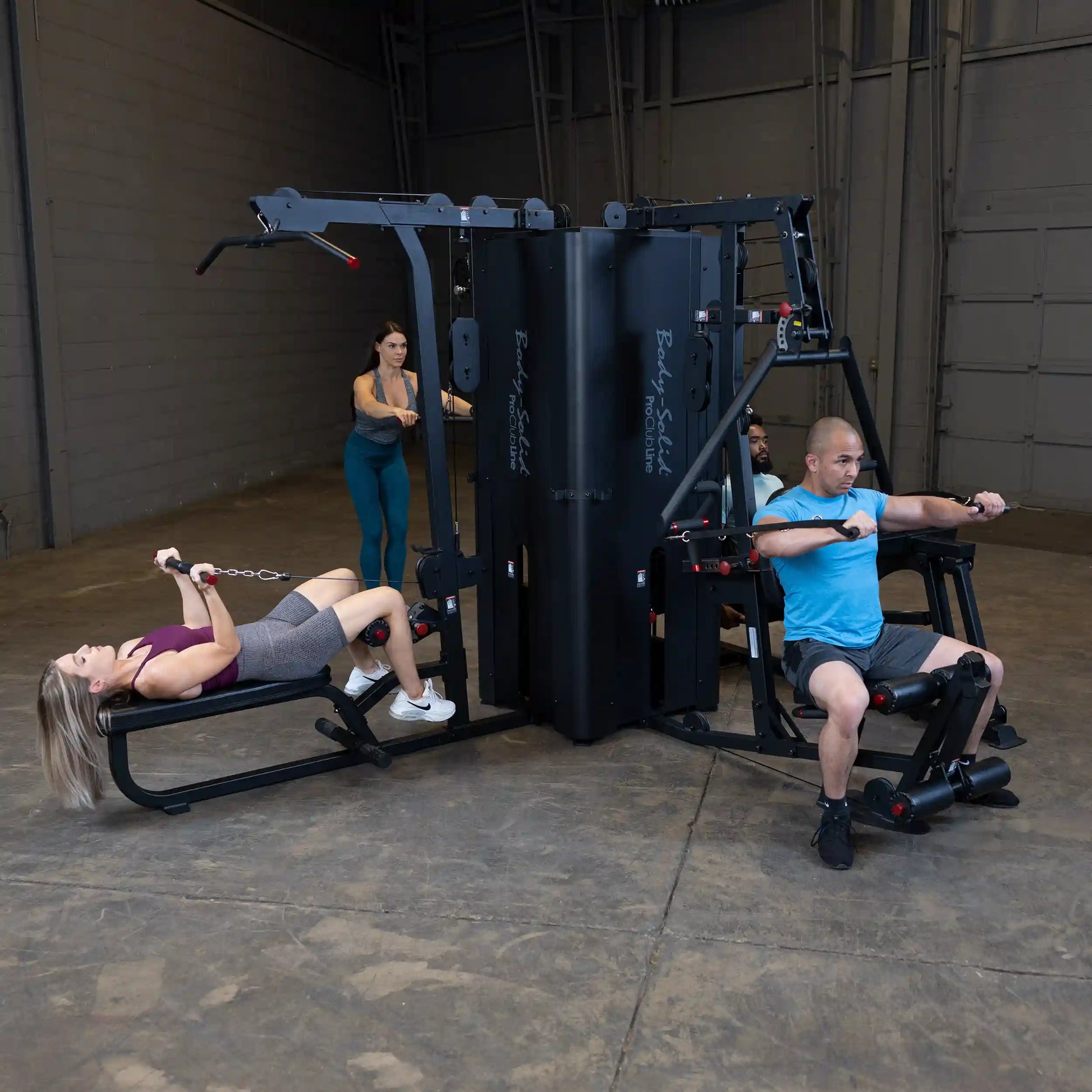 Two individuals exercising on the Body-Solid Pro ClubLine Four-Stack Gym S1000, with one using the rowing machine and the other performing a different exercise, in a spacious gym setting.