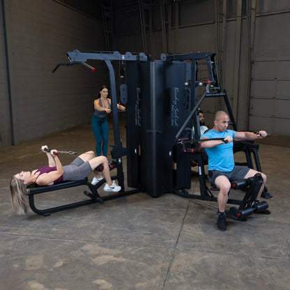 Two individuals exercising on the Body-Solid Pro ClubLine Four-Stack Gym S1000, with one using the rowing machine and the other performing a different exercise, in a spacious gym setting.