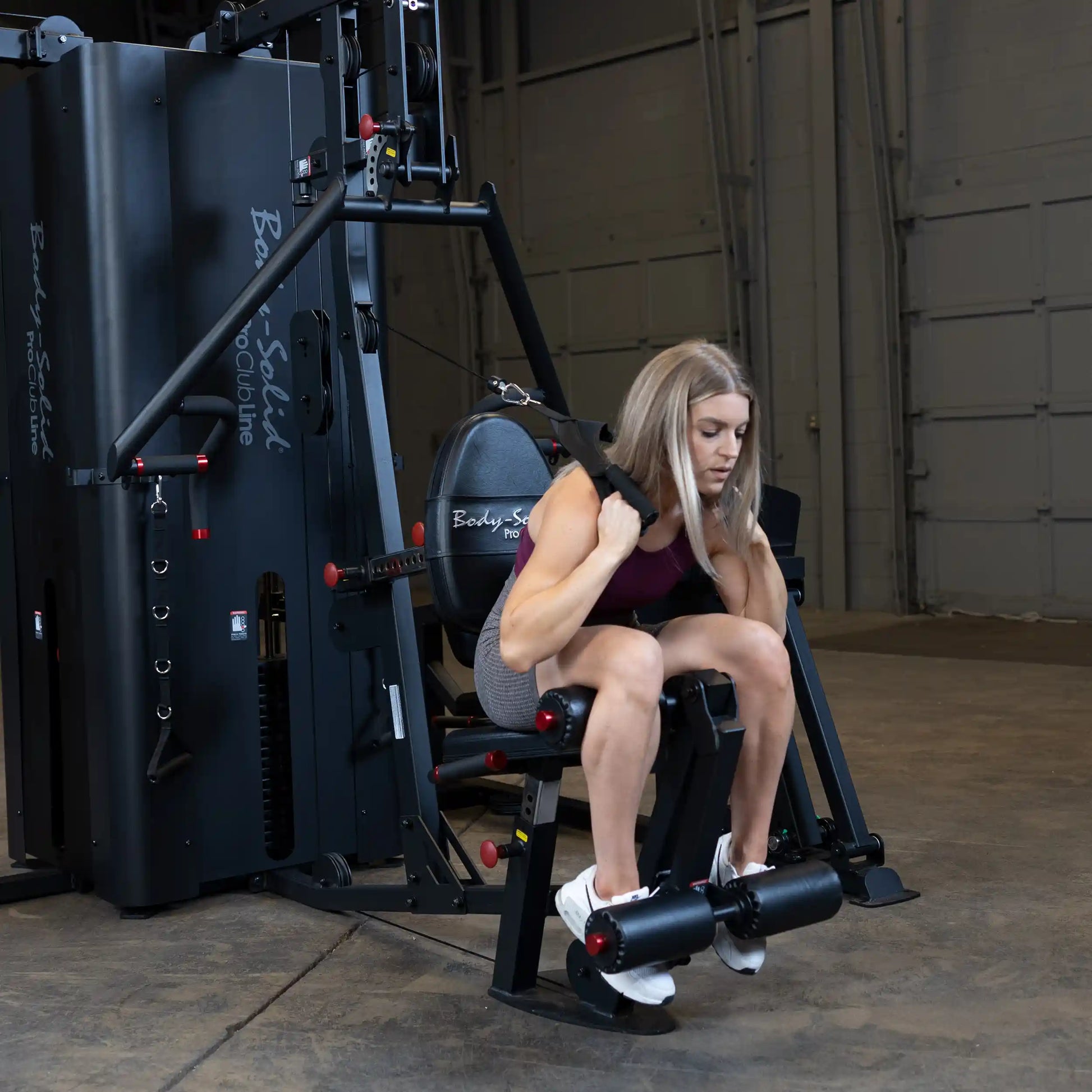A woman using the Body-Solid Pro ClubLine Four-Stack Gym S1000, performing an exercise while seated on the machine in a spacious gym setting.