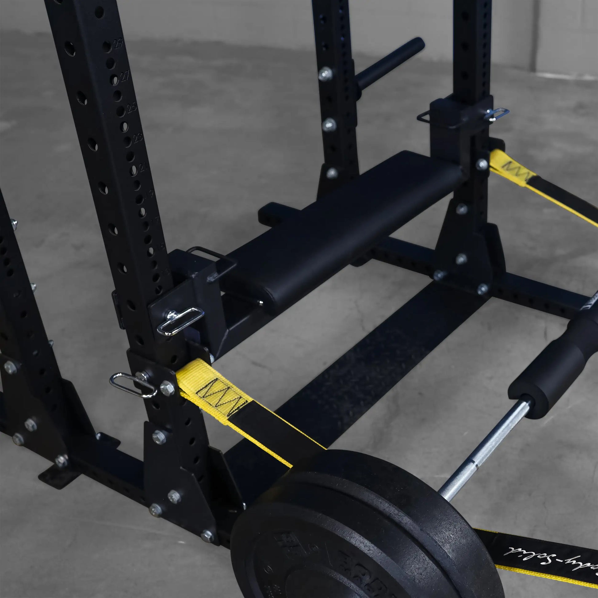 Close-up view of the Body-Solid Pro ClubLine Hip Thrust Attachment SPRHT, featuring a padded surface and yellow resistance bands attached to a sturdy black frame with weights.