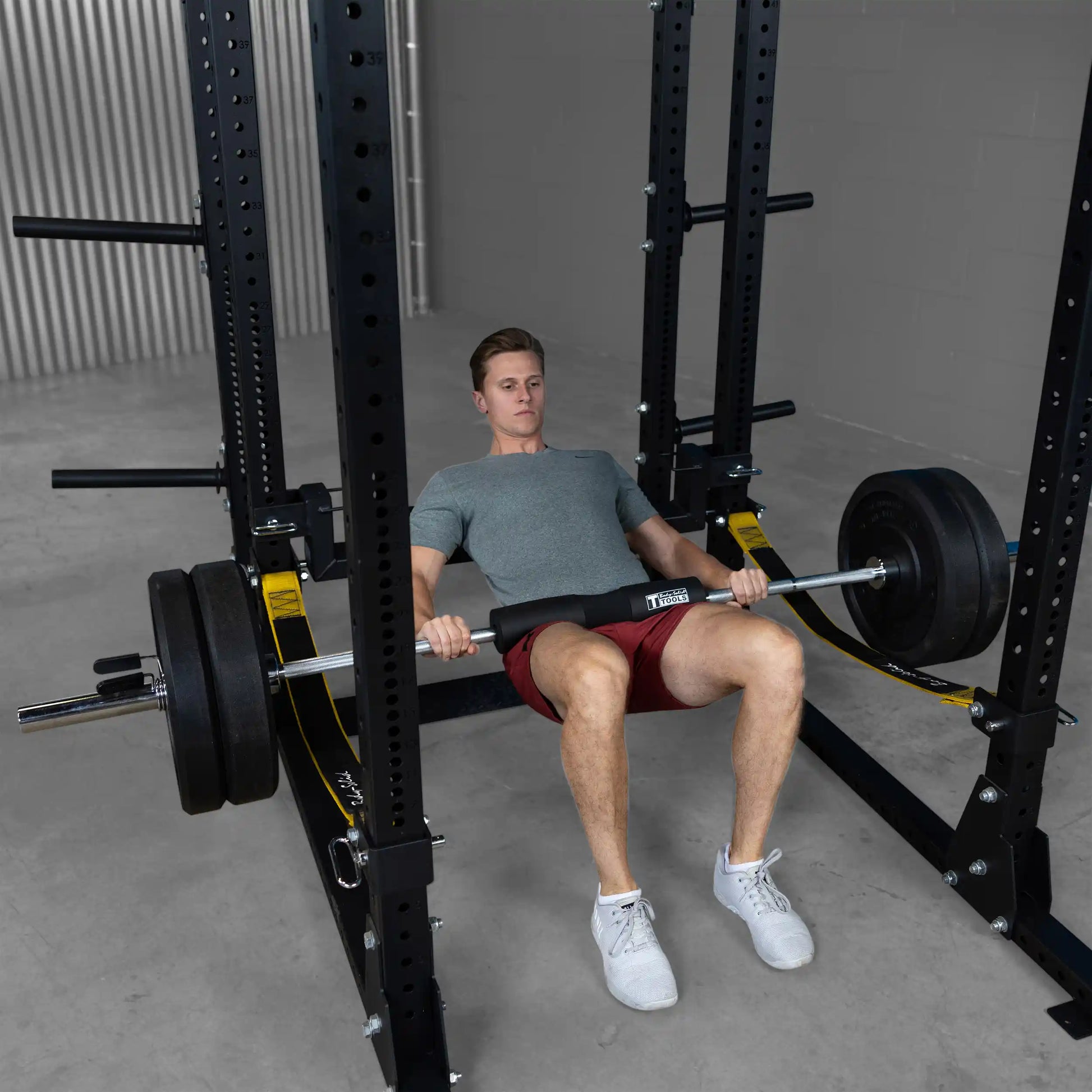 A person using the Body-Solid Pro ClubLine Hip Thrust Attachment SPRHT in a gym setting, performing a hip thrust exercise with a loaded barbell.