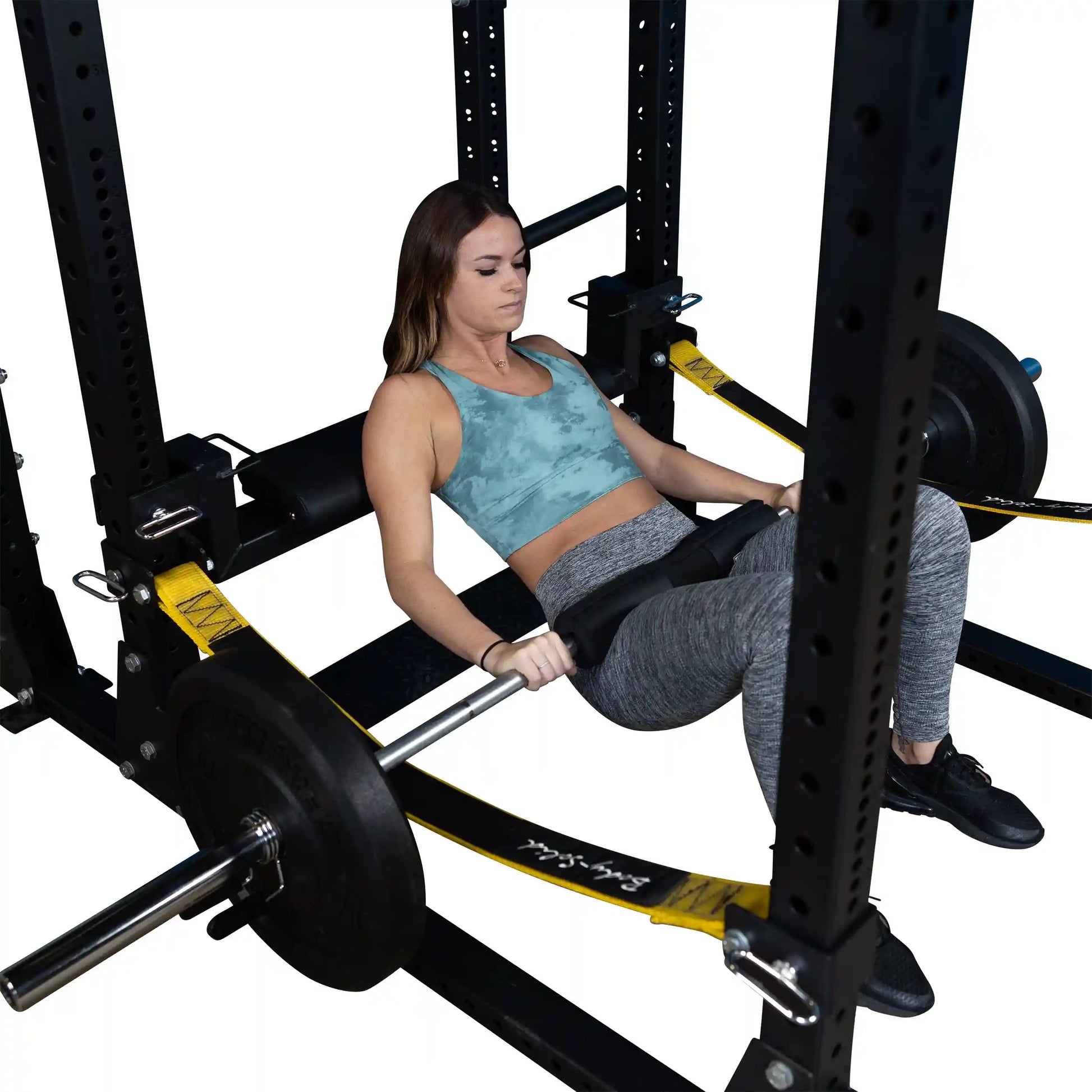 A woman performs a hip thrust using the Body-Solid Pro ClubLine Hip Thrust Attachment SPRHT, positioned in a squat rack with weights on the barbell.