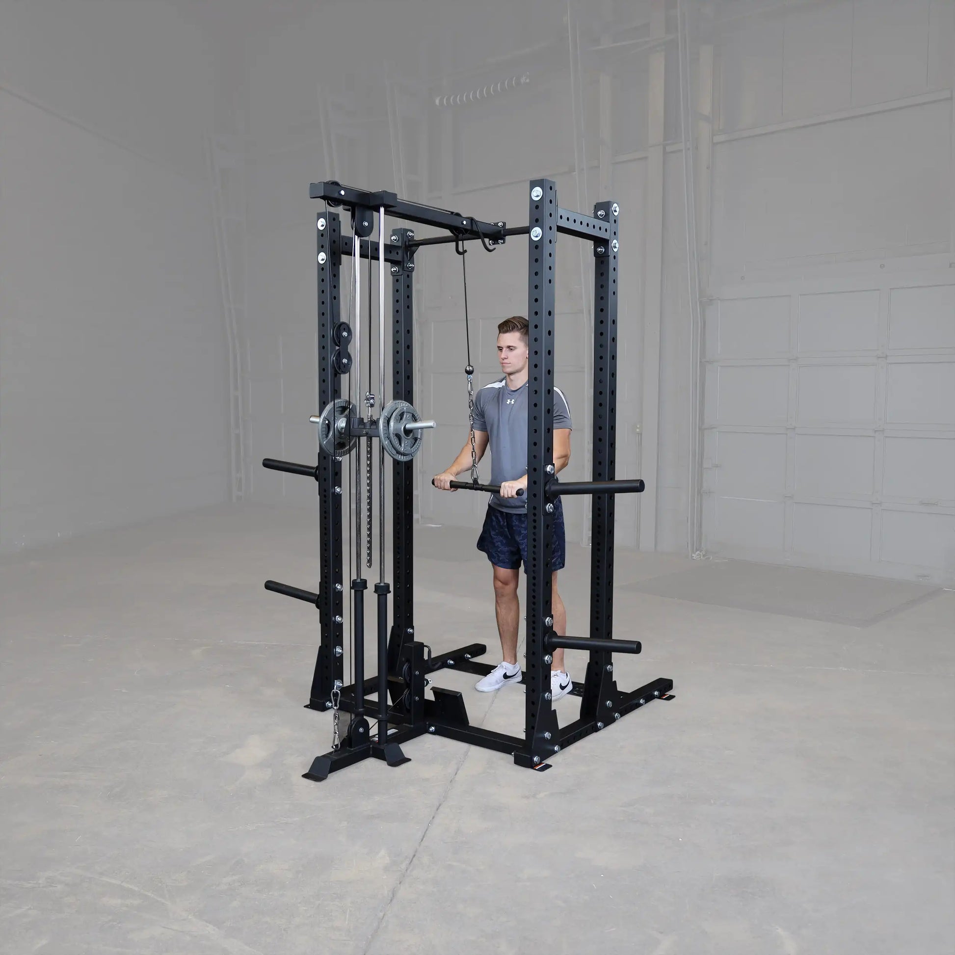 A person using the Body-Solid Pro ClubLine Lat Attachment SPRHLA, standing in front of a weight lifting station in a spacious gym environment.