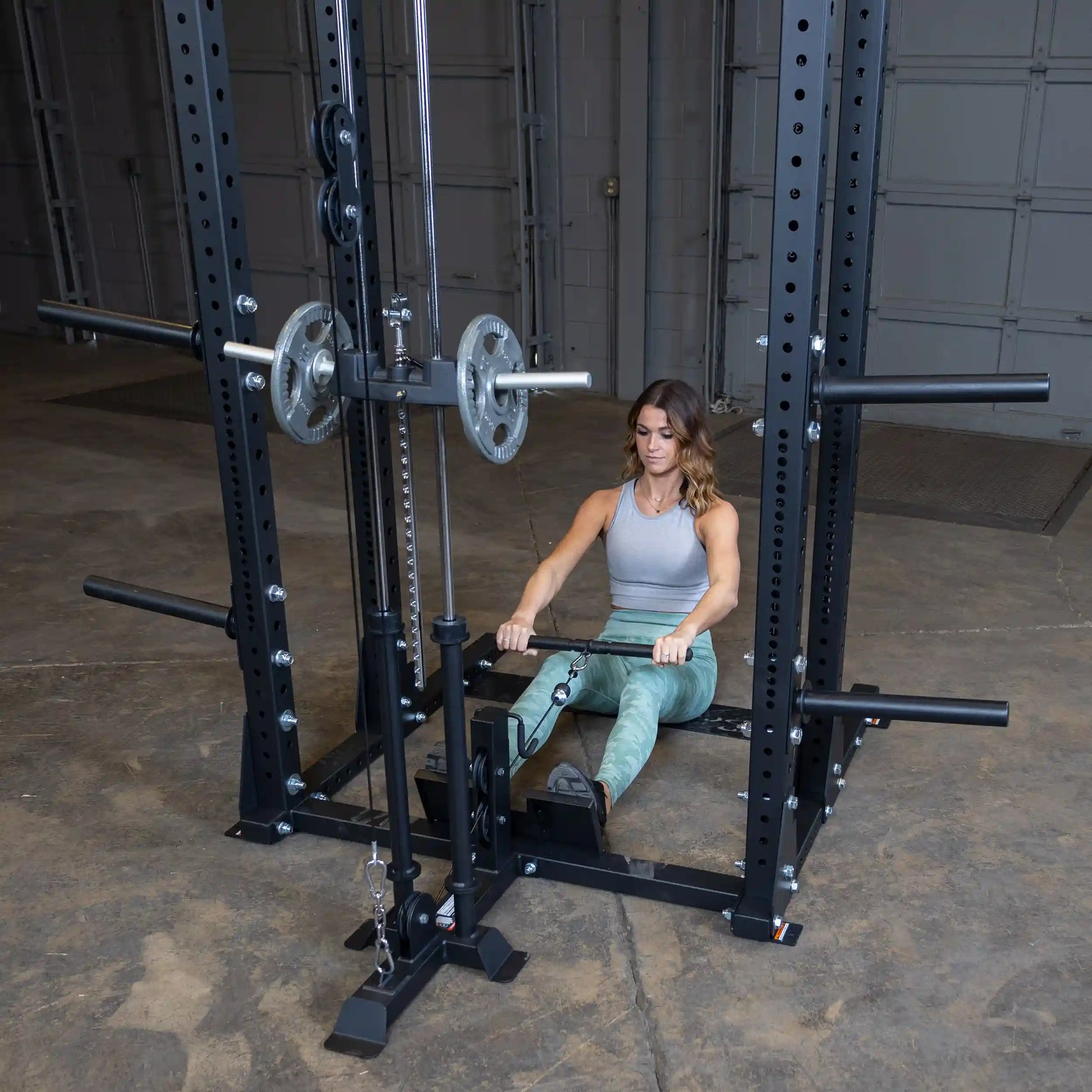 A woman using the Body-Solid Pro ClubLine Lat Attachment SPRHLA, performing a seated rowing exercise with a cable machine in a gym setting.