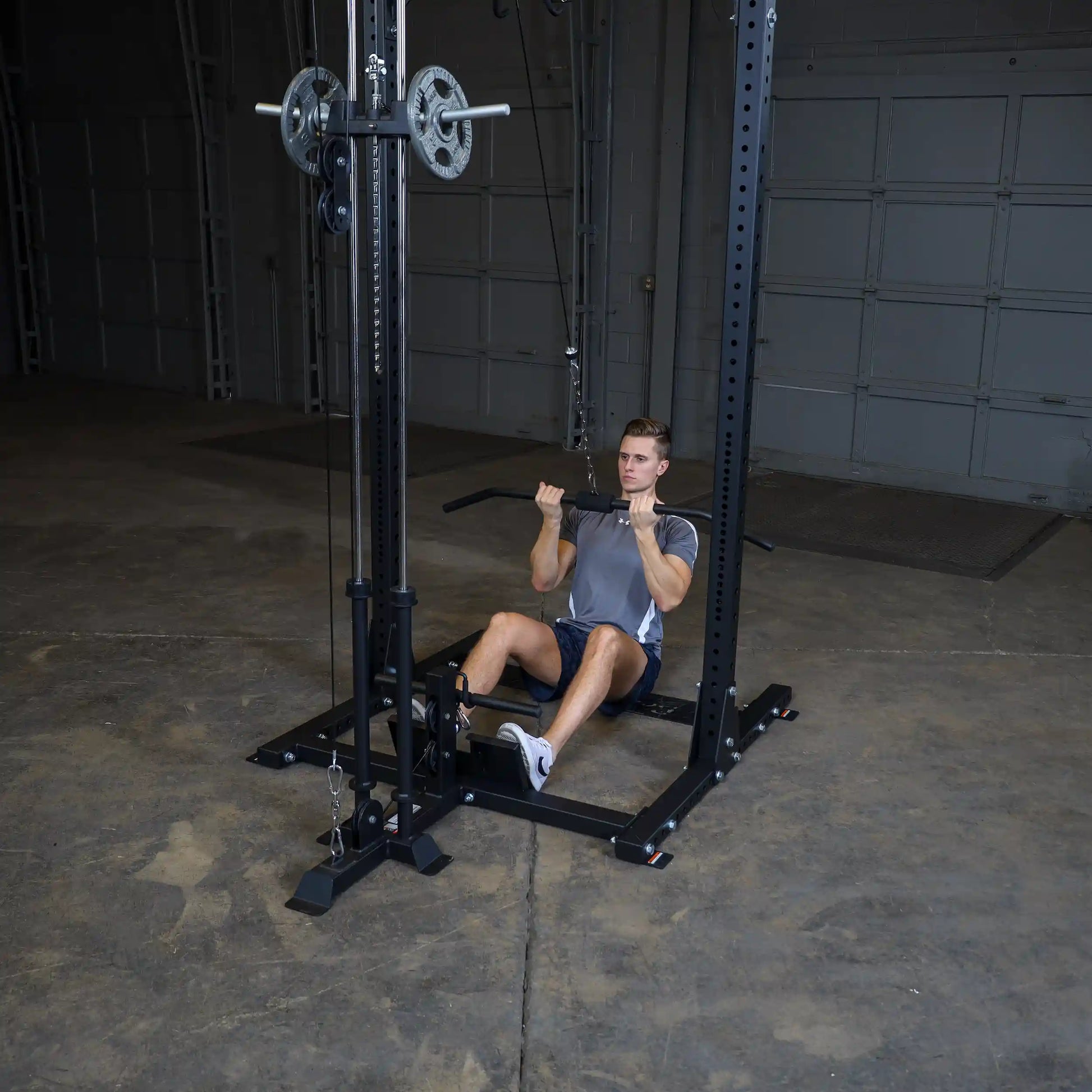 A young man performing a seated row exercise using the Body-Solid Pro ClubLine Lat Attachment SPRHLA in a gym setting with a concrete floor and garage-style background.