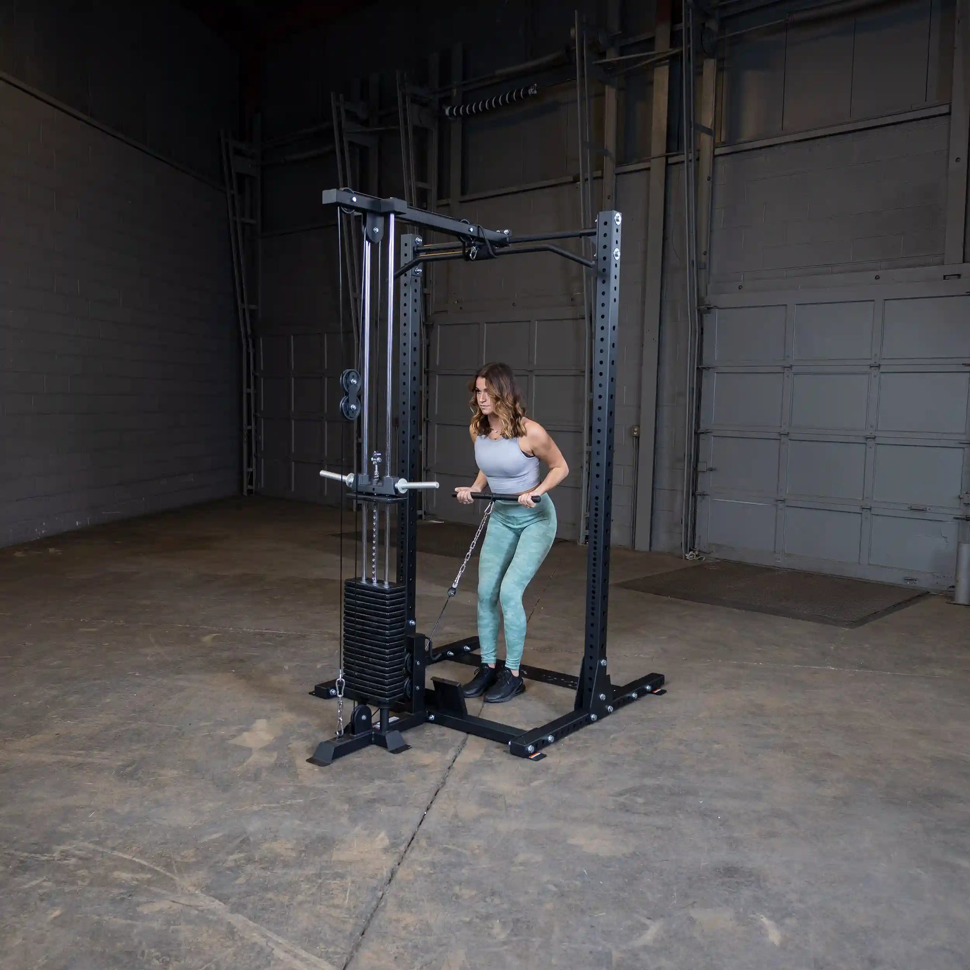 A woman using the Body-Solid Pro ClubLine Lat Attachment SPRHLA in a spacious gym setting, performing a lat pull-down exercise.