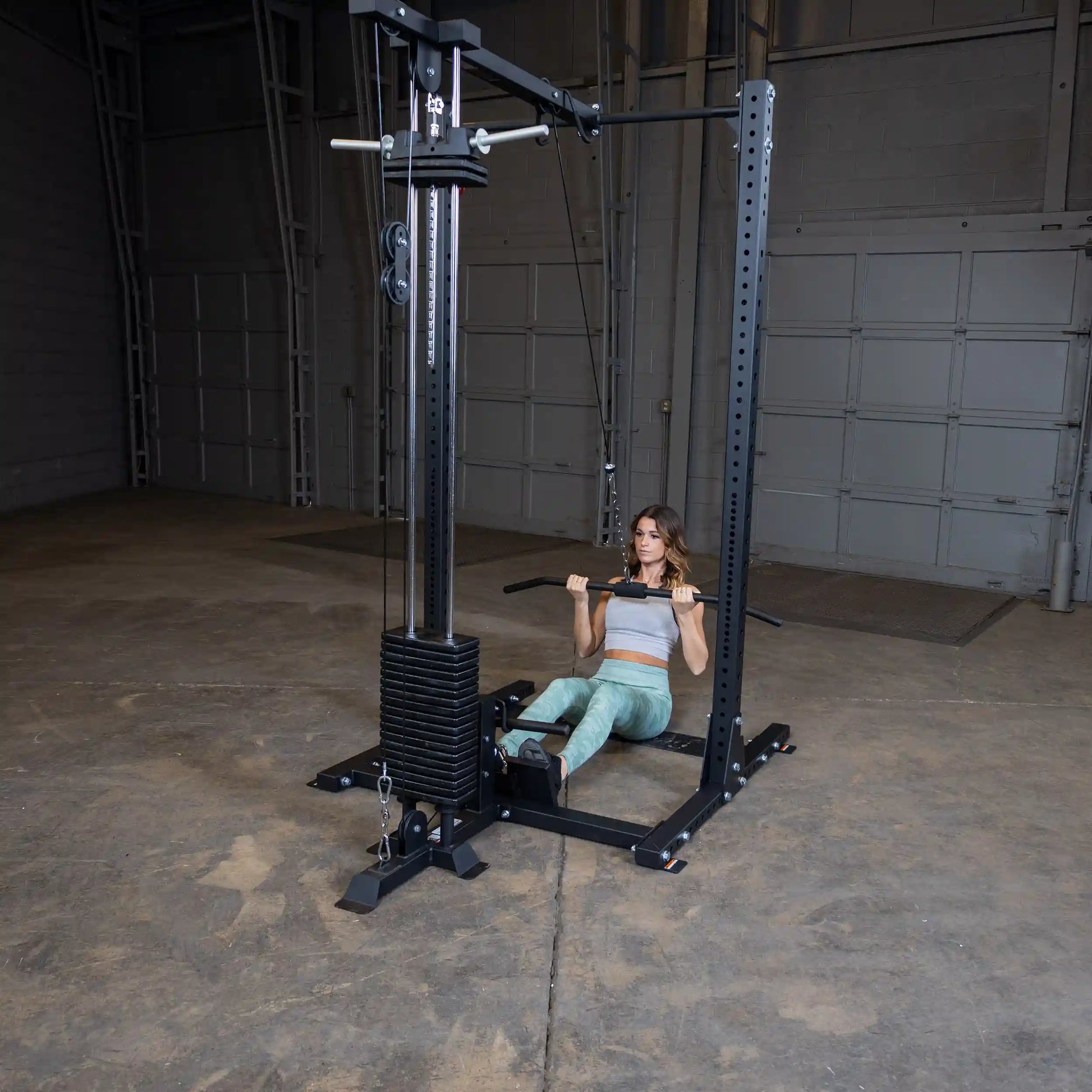 A woman performing a seated row exercise using the Body-Solid Pro ClubLine Lat Attachment SPRHLA in a spacious indoor gym setting.
