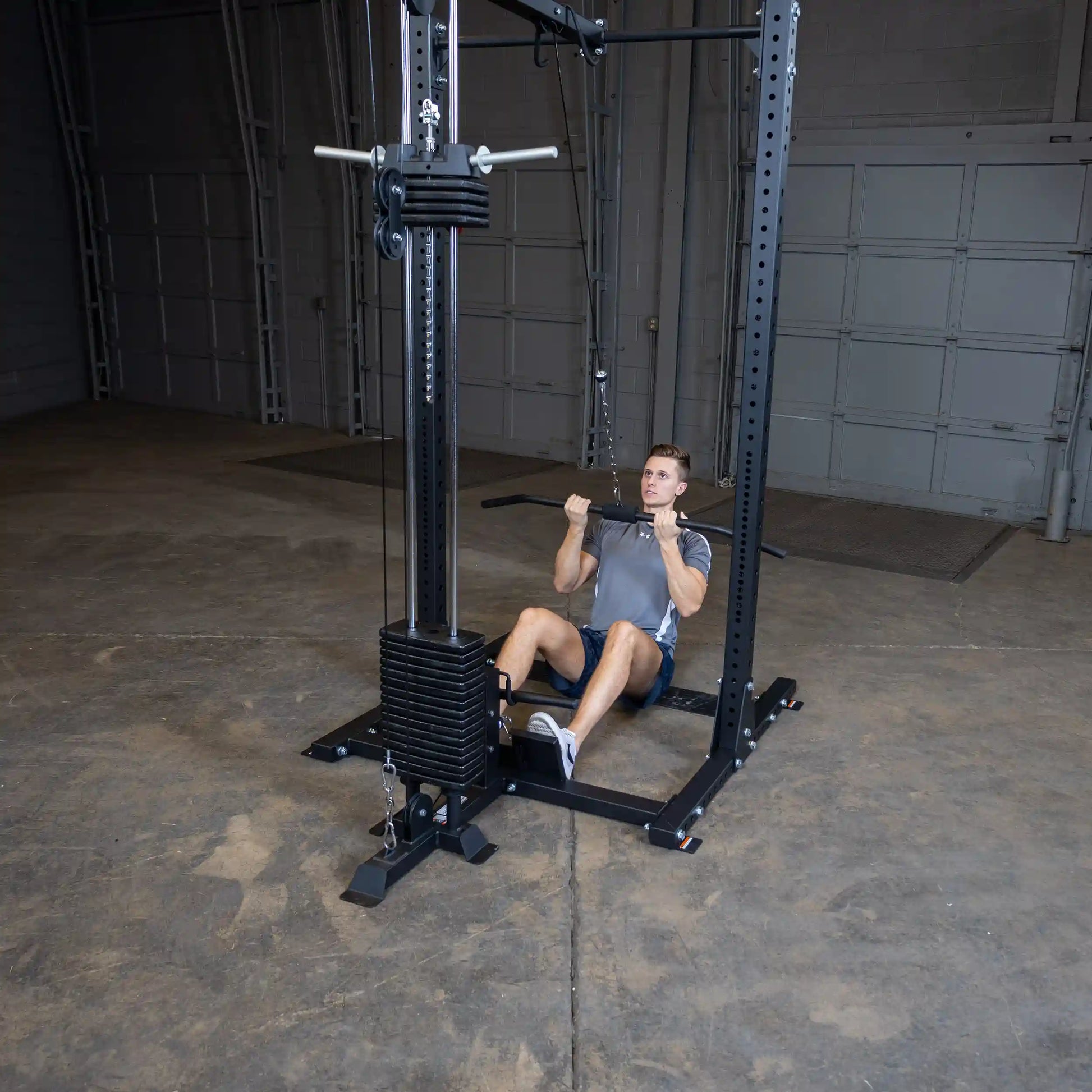A person performing a lat pulldown exercise using the Body-Solid Pro ClubLine Lat Attachment SPRHLA in a spacious gym setting with a concrete floor.