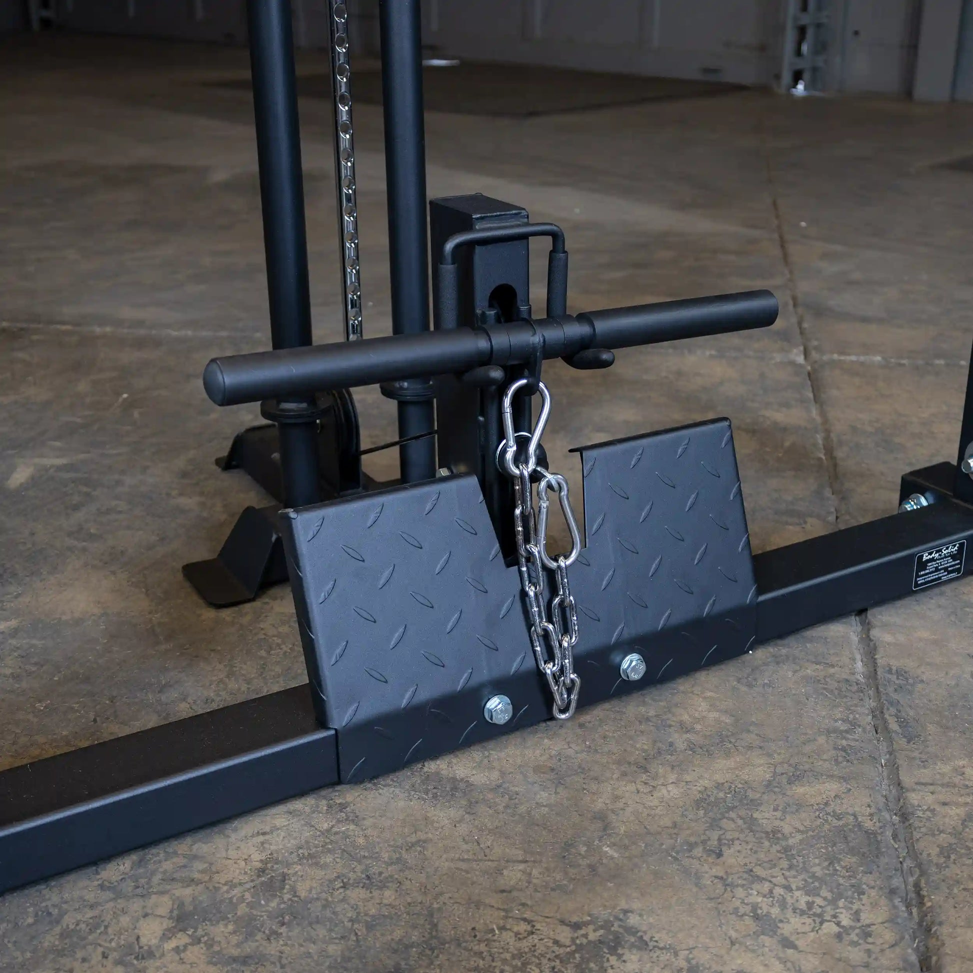 Close-up of the Body-Solid Pro ClubLine Lat Attachment SPRHLA, featuring a black frame, a padded handlebar, and a chain attachment on a textured platform, set against a concrete floor.