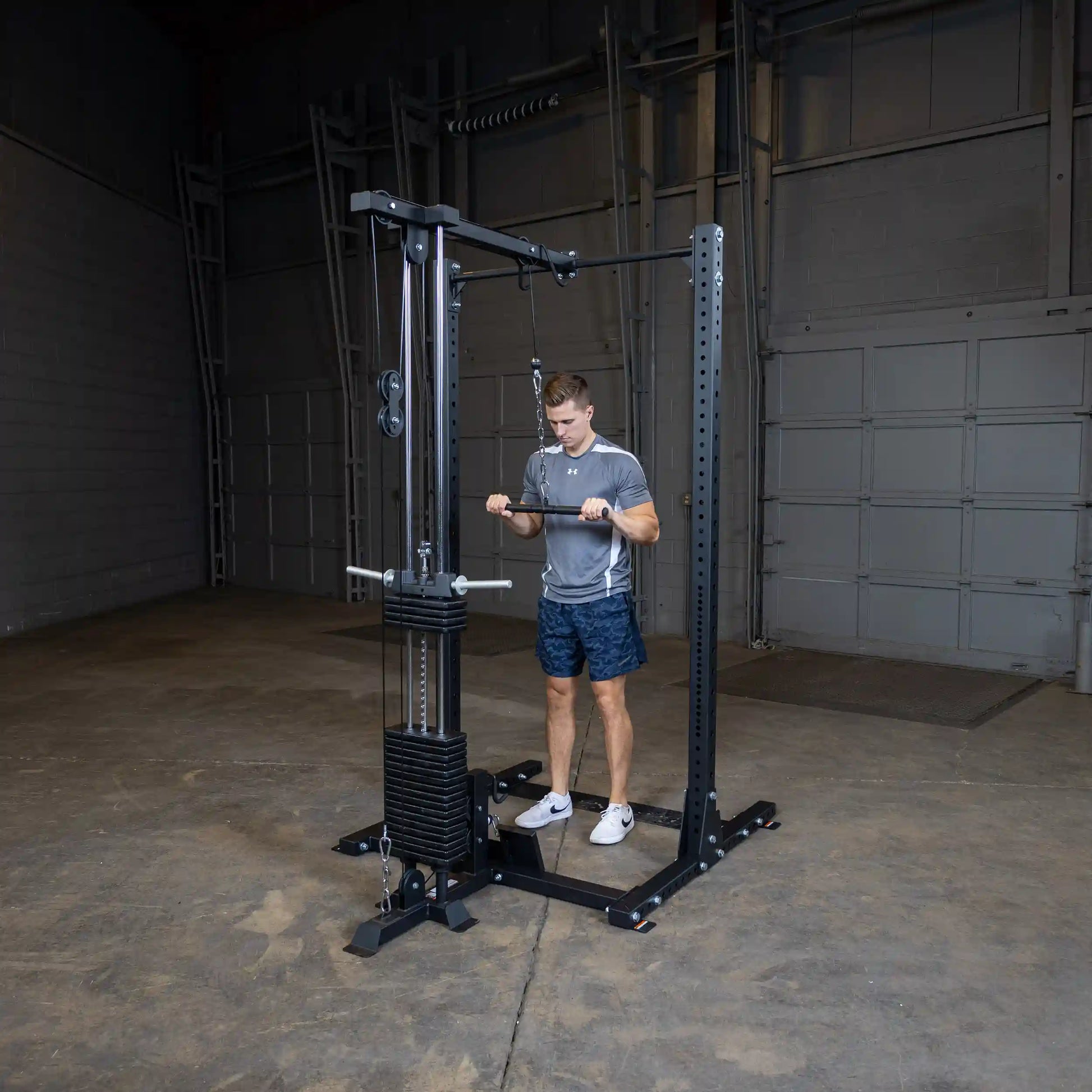 A person using the Body-Solid Pro ClubLine Lat Attachment SPRHLA in a gym setting, performing an exercise while standing on a gym floor.