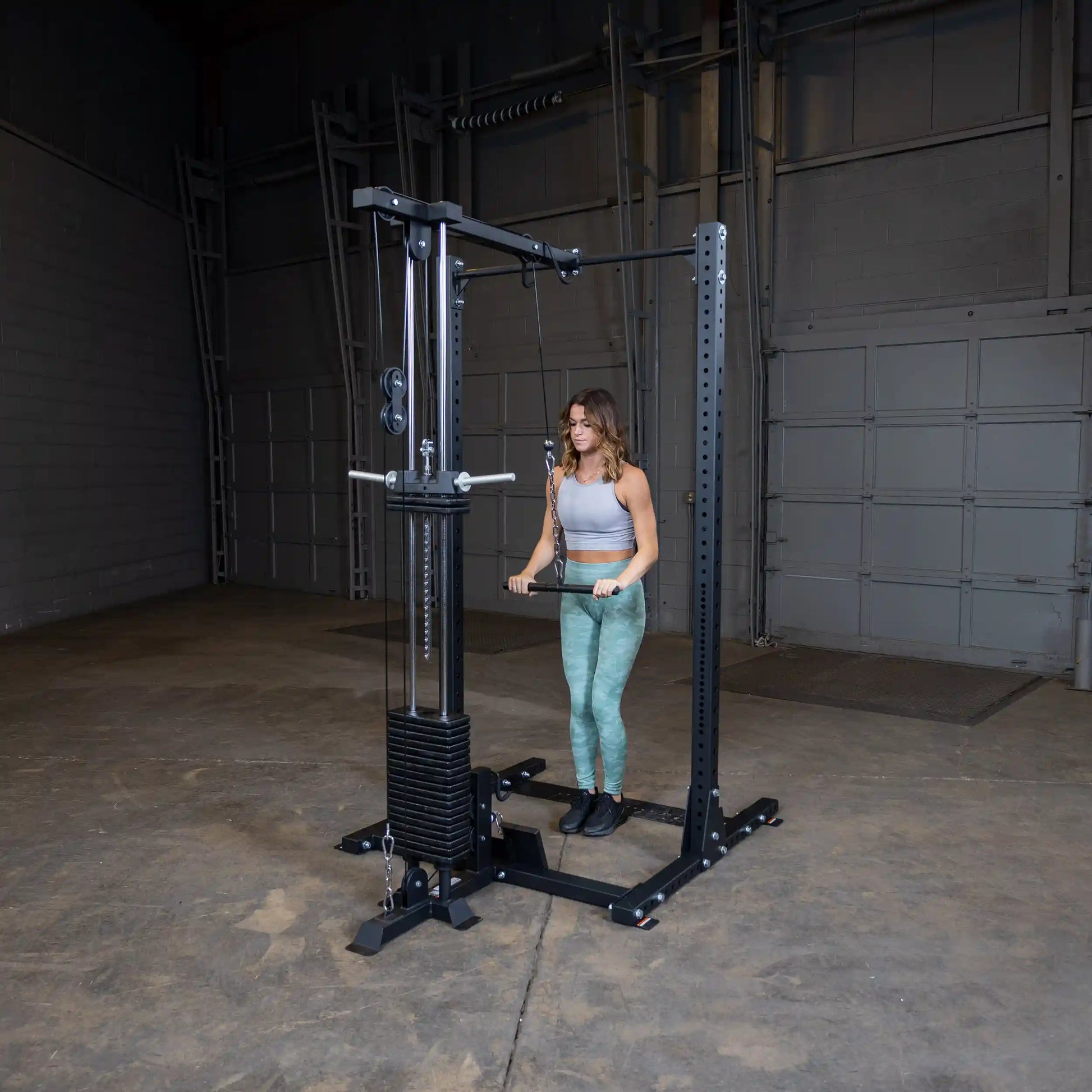 A woman using the Body-Solid Pro ClubLine Lat Attachment SPRHLA in a gym setting, performing a lat pull exercise with weights.