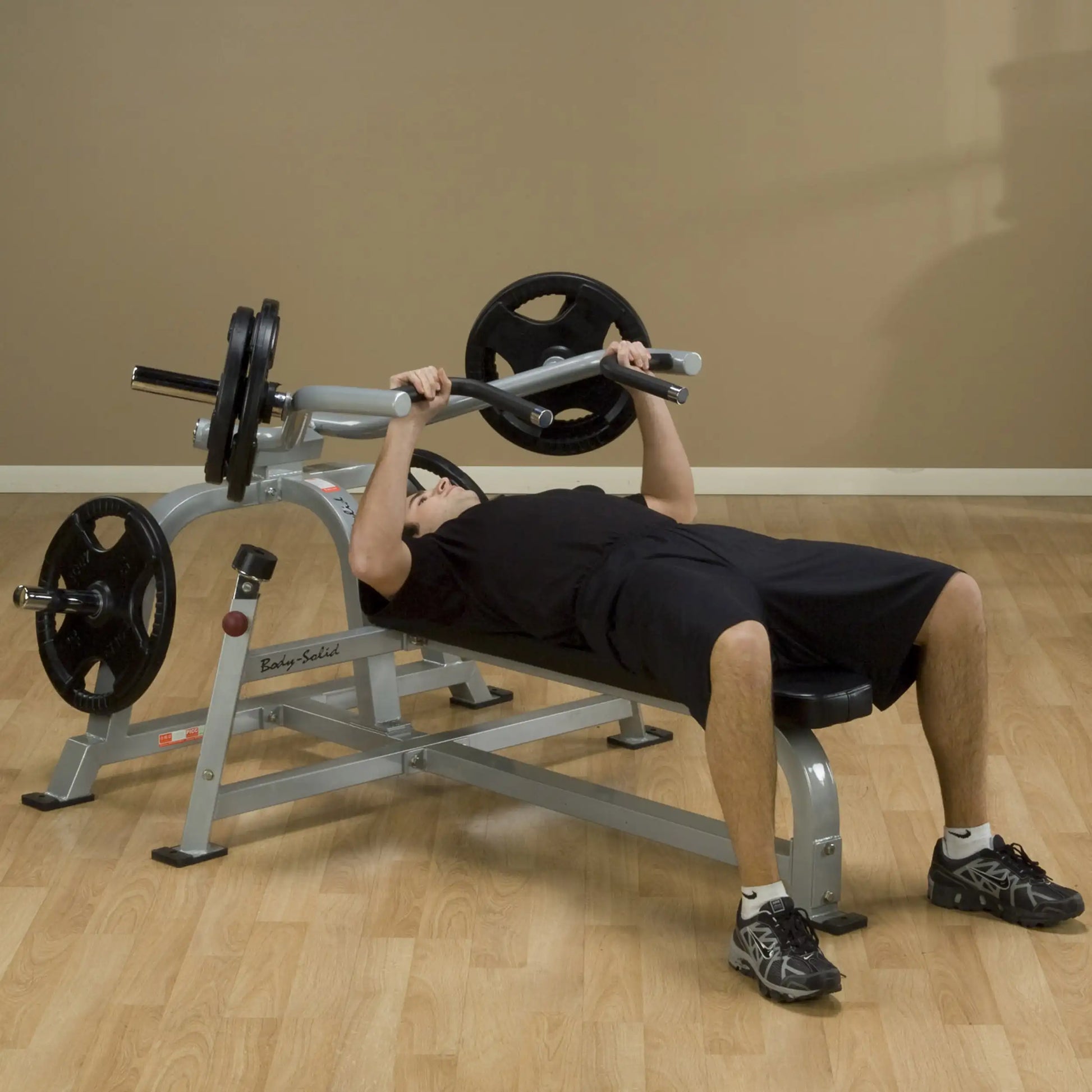 A person performing a bench press on the Body-Solid Pro ClubLine Leverage Bench Press LVBP, with weights on the bar, in a fitness setting.