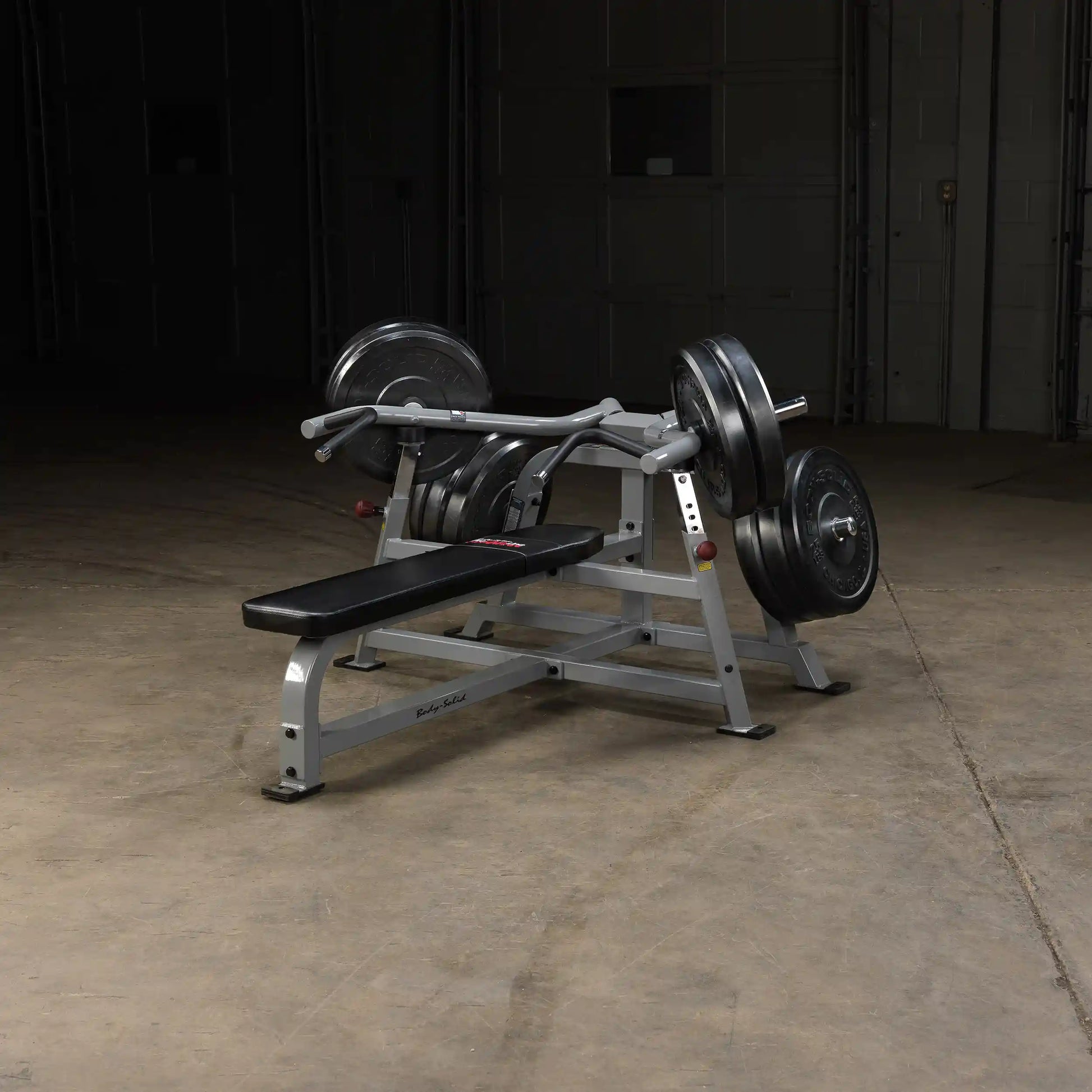 Body-Solid Pro ClubLine Leverage Bench Press LVBP with weights, positioned on a concrete floor in a dimly lit environment.