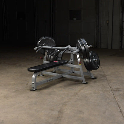 Body-Solid Pro ClubLine Leverage Bench Press LVBP with weights, positioned on a concrete floor in a dimly lit environment.