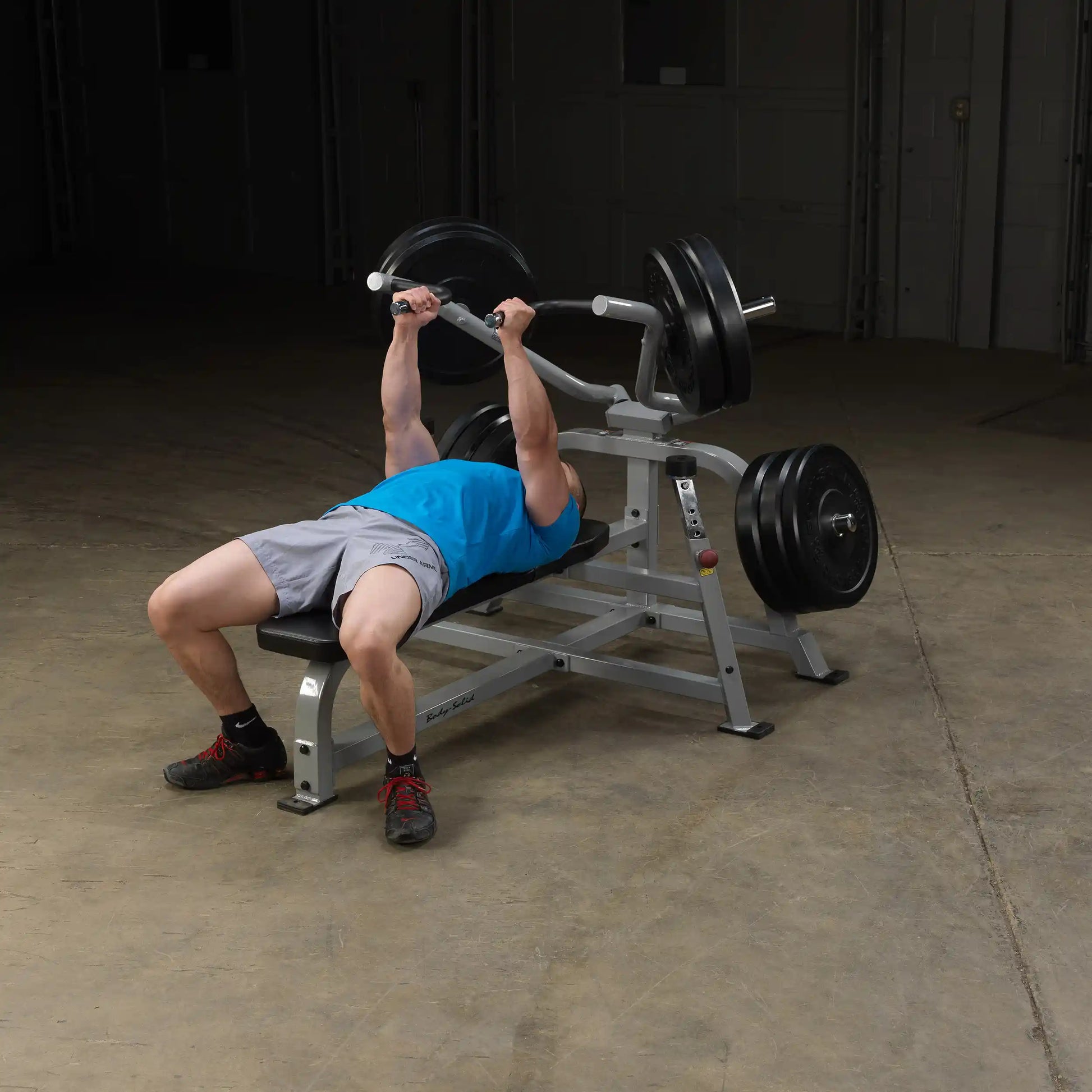 A person performing a bench press on the Body-Solid Pro ClubLine Leverage Bench Press LVBP, with weights on either side, in an industrial gym setting.