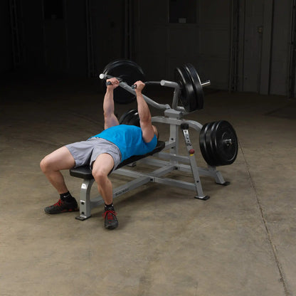 A person performing a bench press on the Body-Solid Pro ClubLine Leverage Bench Press LVBP, with weights on either side, in an industrial gym setting.