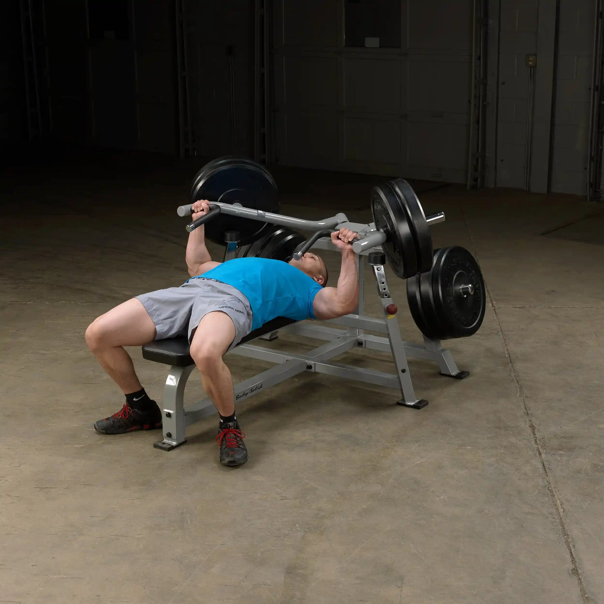 A person performing a bench press on the Body-Solid Pro ClubLine Leverage Bench Press LVBP, lifting a weighted barbell in a gym setting.