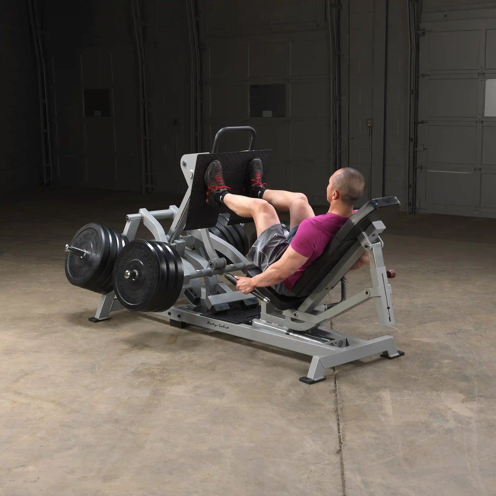 A person using the Body-Solid Pro ClubLine Leverage Horizontal Leg Press Machine LVLP in a gym setting, performing leg presses with weights on the machine.