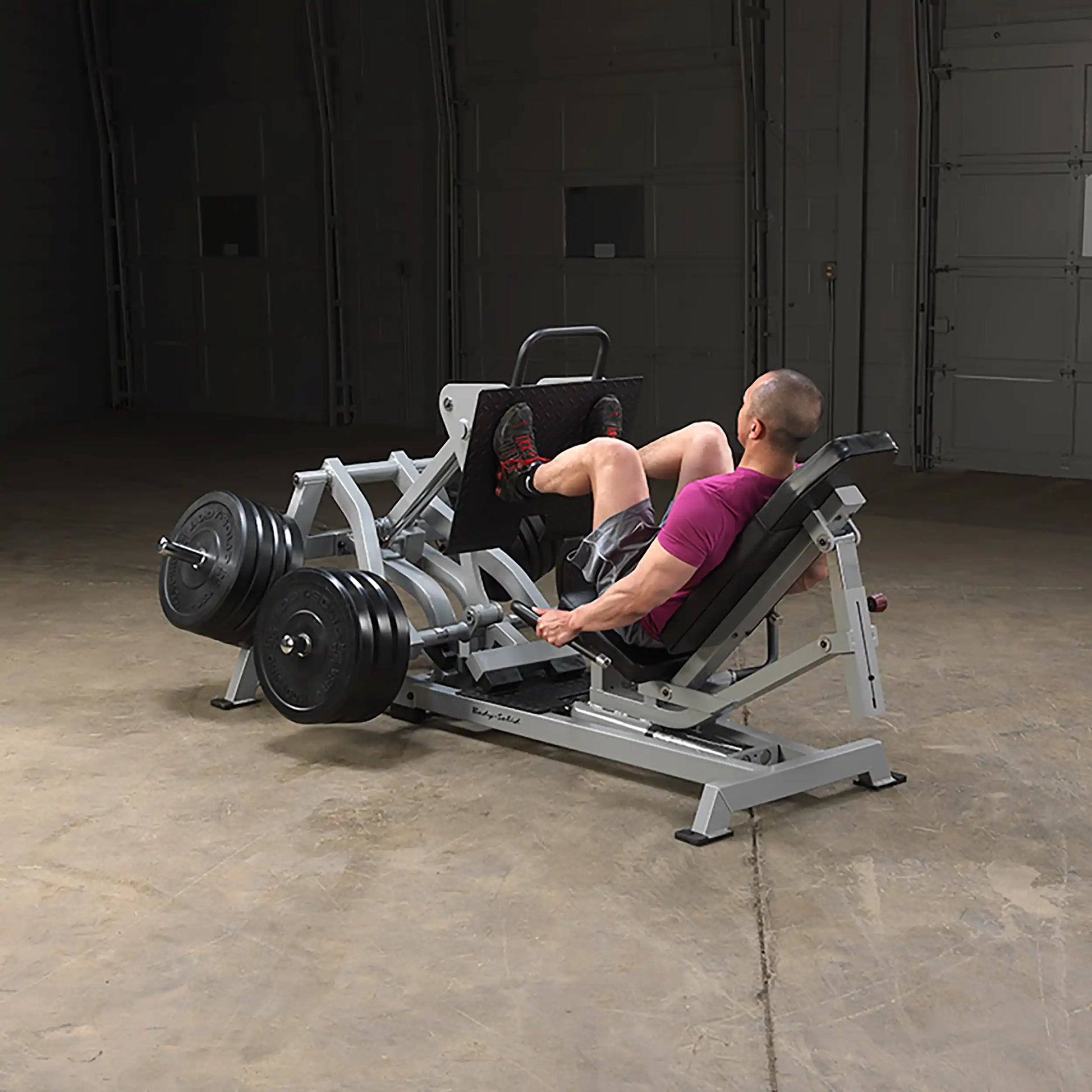 A person using the Body-Solid Pro ClubLine Leverage Horizontal Leg Press Machine LVLP in a gym setting, performing leg press exercises with weights.