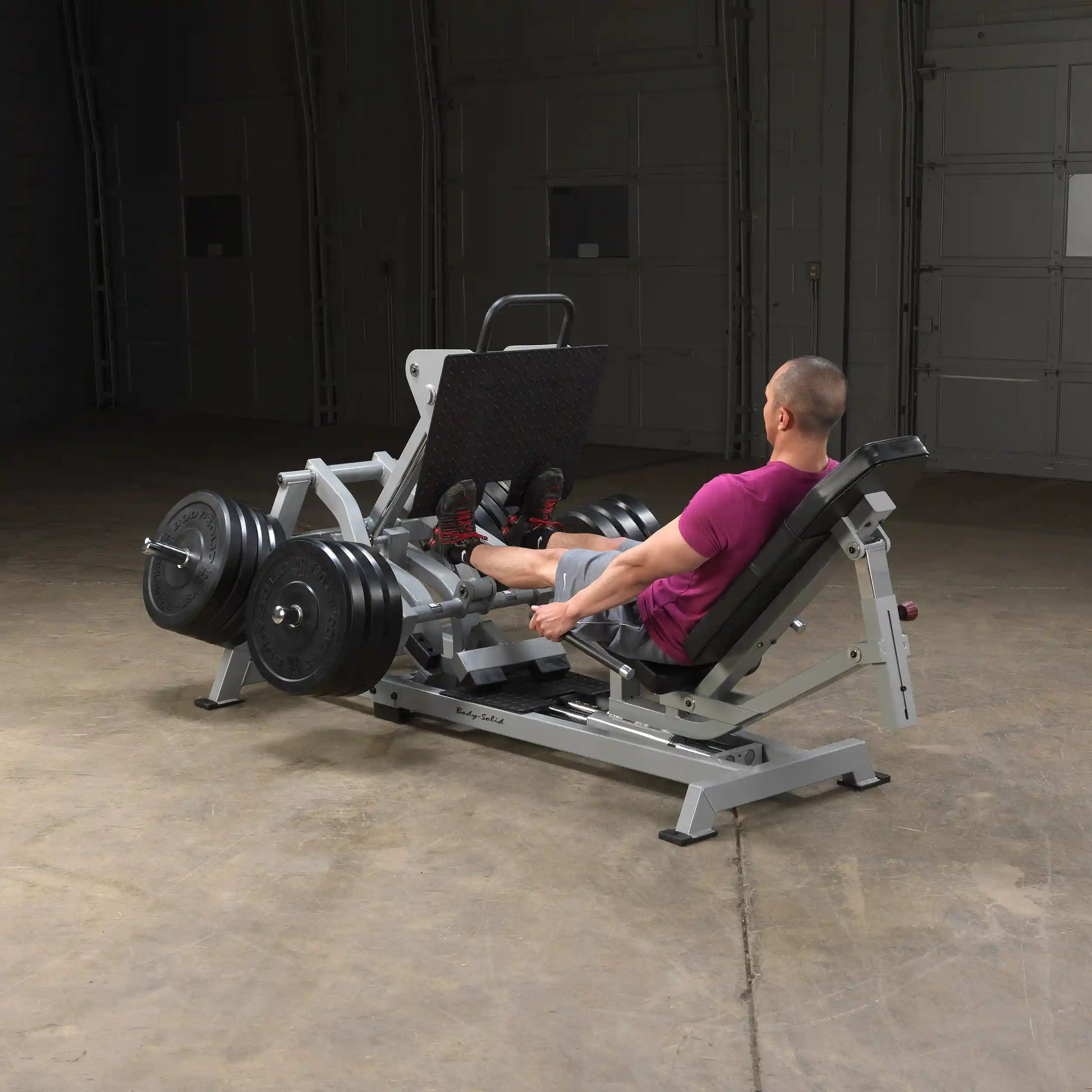 A person using the Body-Solid Pro ClubLine Leverage Horizontal Leg Press Machine LVLP in a gym setting, focusing on leg workouts with weights attached.