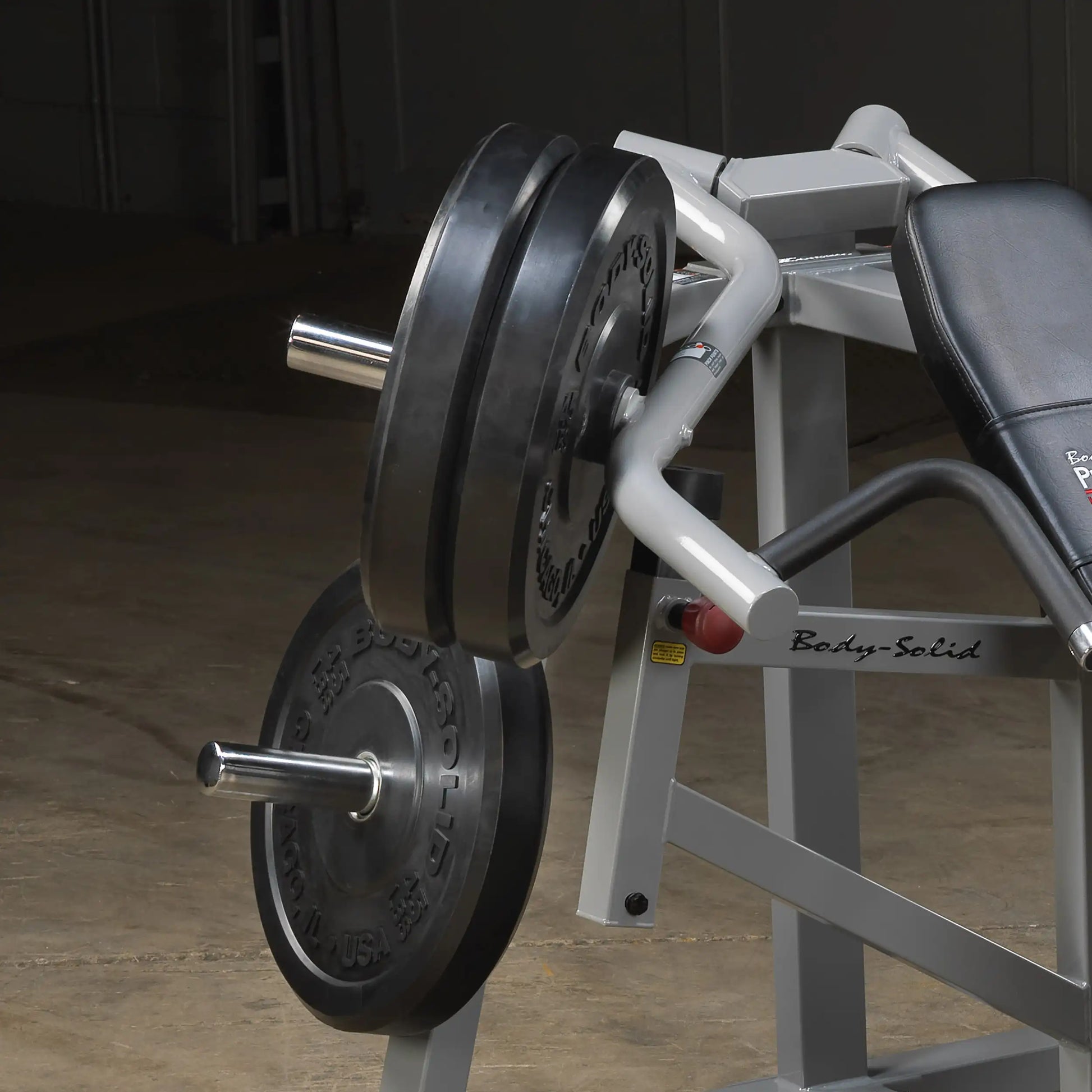 Close-up of the Body-Solid Pro ClubLine Leverage Incline Press LVIP, featuring weight plates and a padded seat, set in an industrial gym environment.