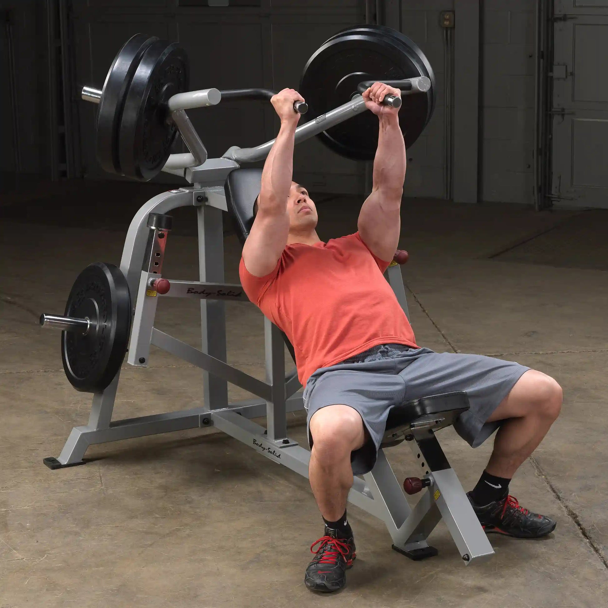 A person performing an exercise on the Body-Solid Pro ClubLine Leverage Incline Press LVIP, using a barbell with weights in a gym setting.